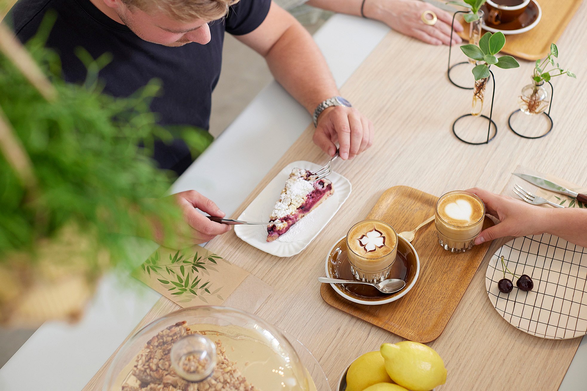   Close-up van een AMAi-tafel met een houten blad, waar mensen genieten van eten en drinken.