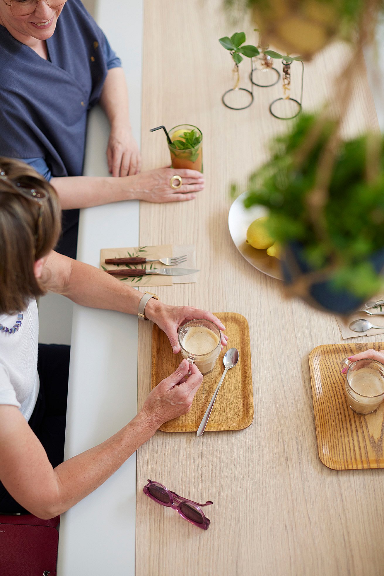   Klanten zitten aan een lange AMAi-tafel met tiki-stoelen in de koffiebar en genieten van een drankje in een ontspannen café-sfeer.