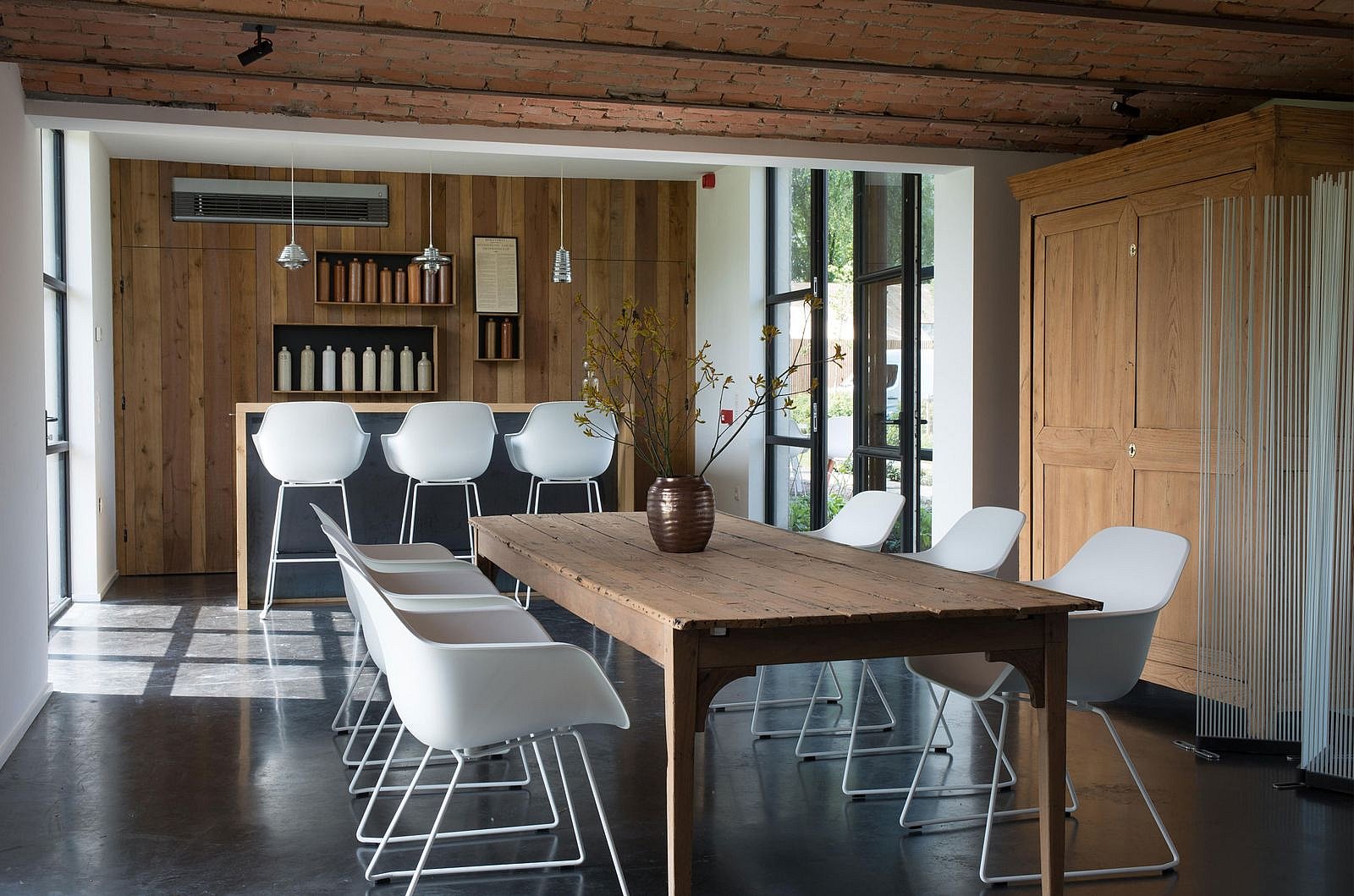 Intérieur d'une grange contemporaine rénovée, avec poutres apparentes, une table entourée de chaises de capitaine blanches et une douce lumière naturelle inondant l'espace rustique.