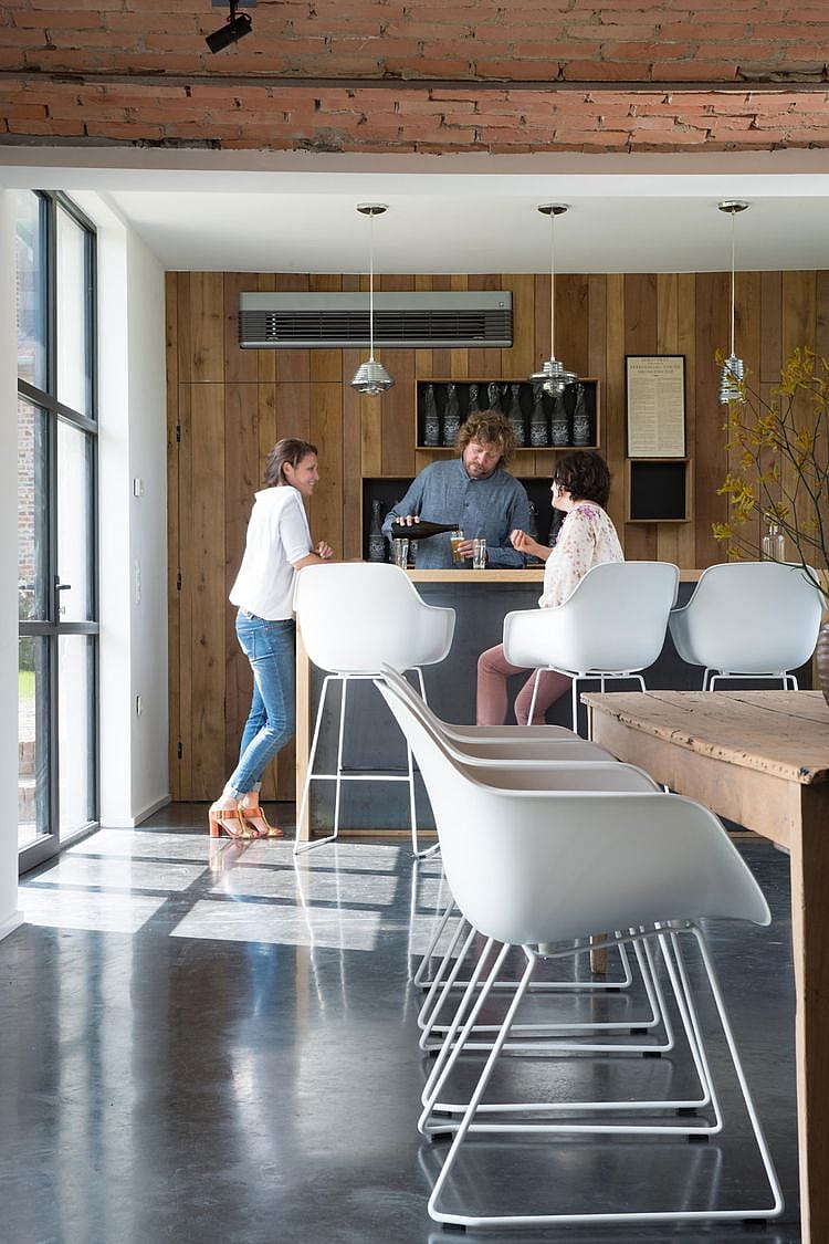 Ruim interieur van de schuur met donkere houten wanden en plafondbalken, met een grote eettafel en witte Captain's Chairs, opgesteld voor gezellige bijeenkomsten.