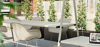 Moderne buitenkantoorruimte met lange AMAi-tafels, witte Captain's-stoelen en een stoffen zonnescherm, omgeven door plantenbakken en groen.