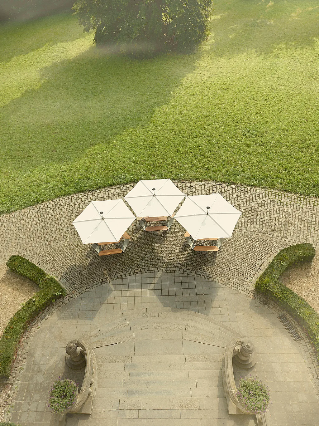 Castle garden terrace in Diksmuide with modern triangular Anker picnic tables and hexagonal Inumbrina parasols set among greenery and historic architecture.