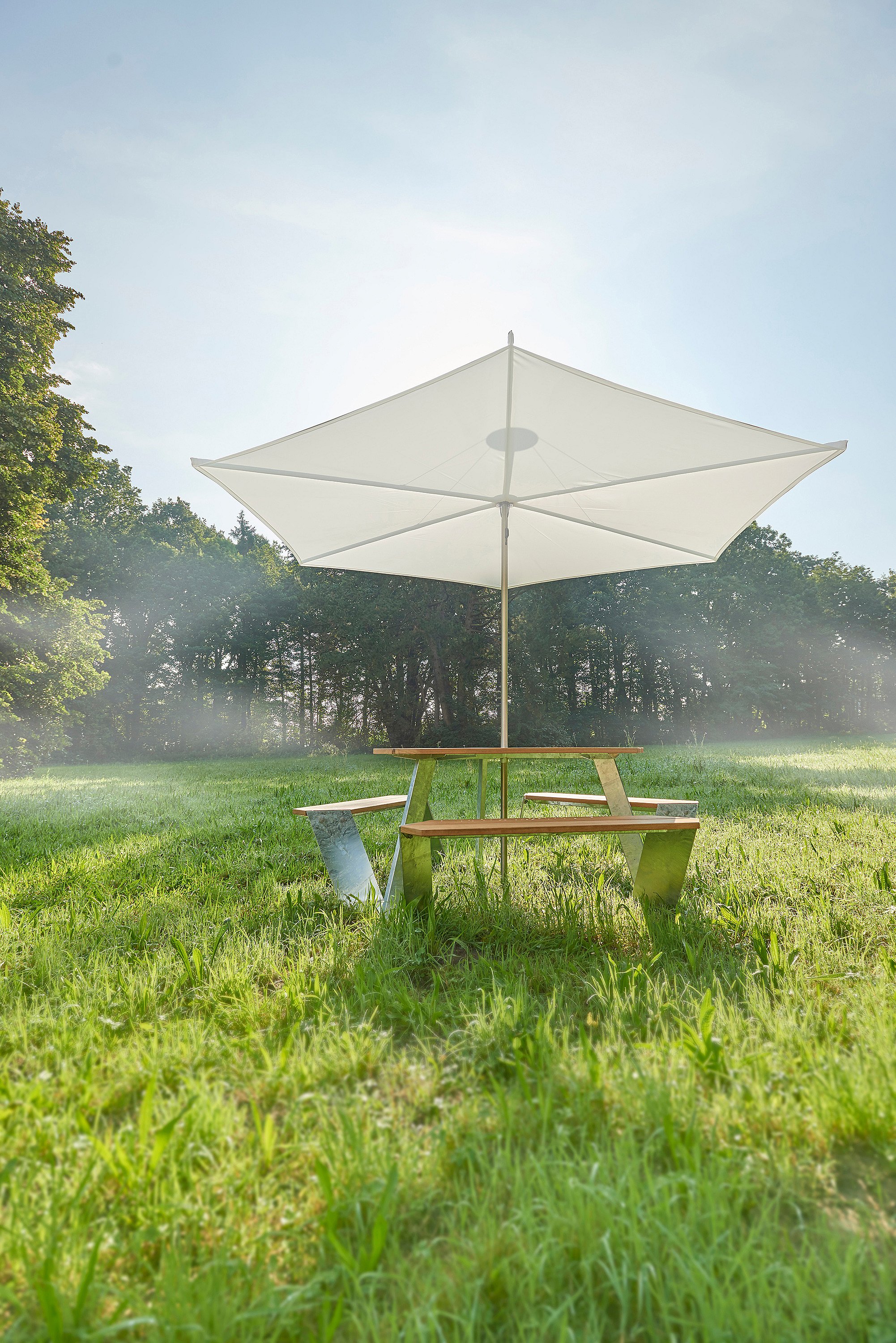   Gros plan sur une table de pique-nique triangulaire Anker avec plateau en bois et bancs intégrés, placée sous un parasol Inumbrina flottant.