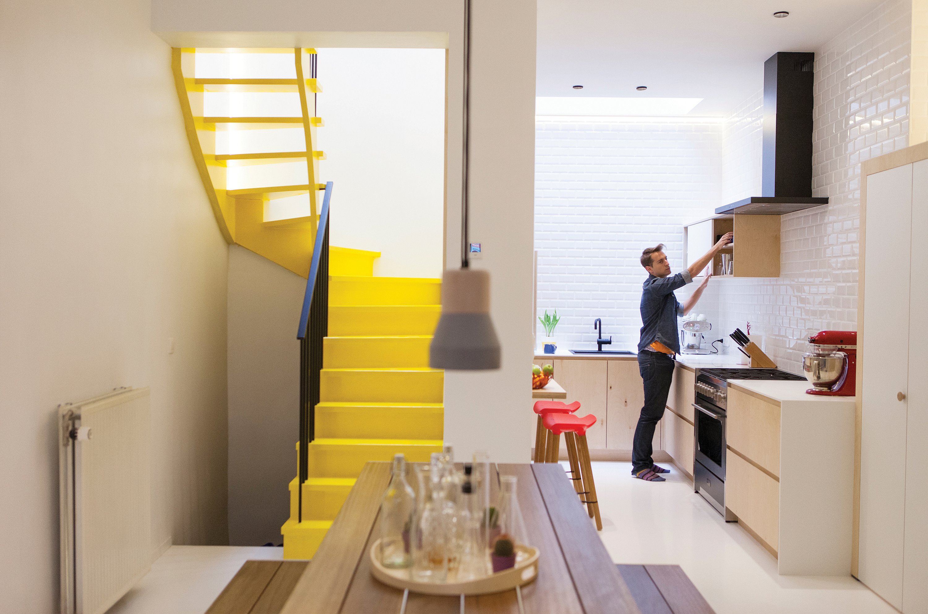 Intérieur blanc lumineux d'une maison de ville moderne à Gand, avec un escalier jaune et une table de pique-nique Hopper en bois faisant office d'espace central pour les repas et les réunions.