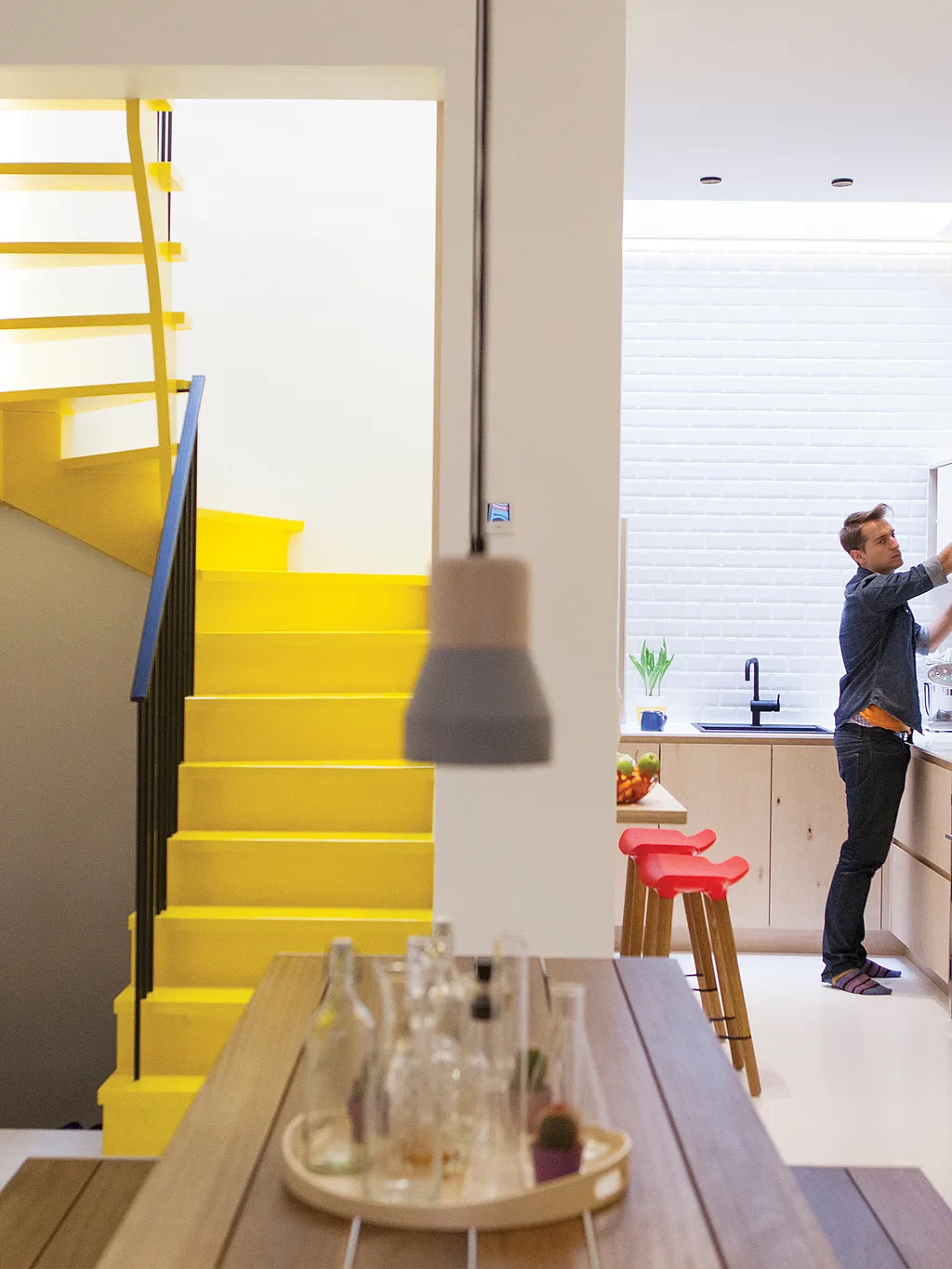 Intérieur blanc lumineux d'une maison de ville moderne à Gand, avec un escalier jaune et une table de pique-nique Hopper en bois faisant office d'espace central pour les repas et les réunions.