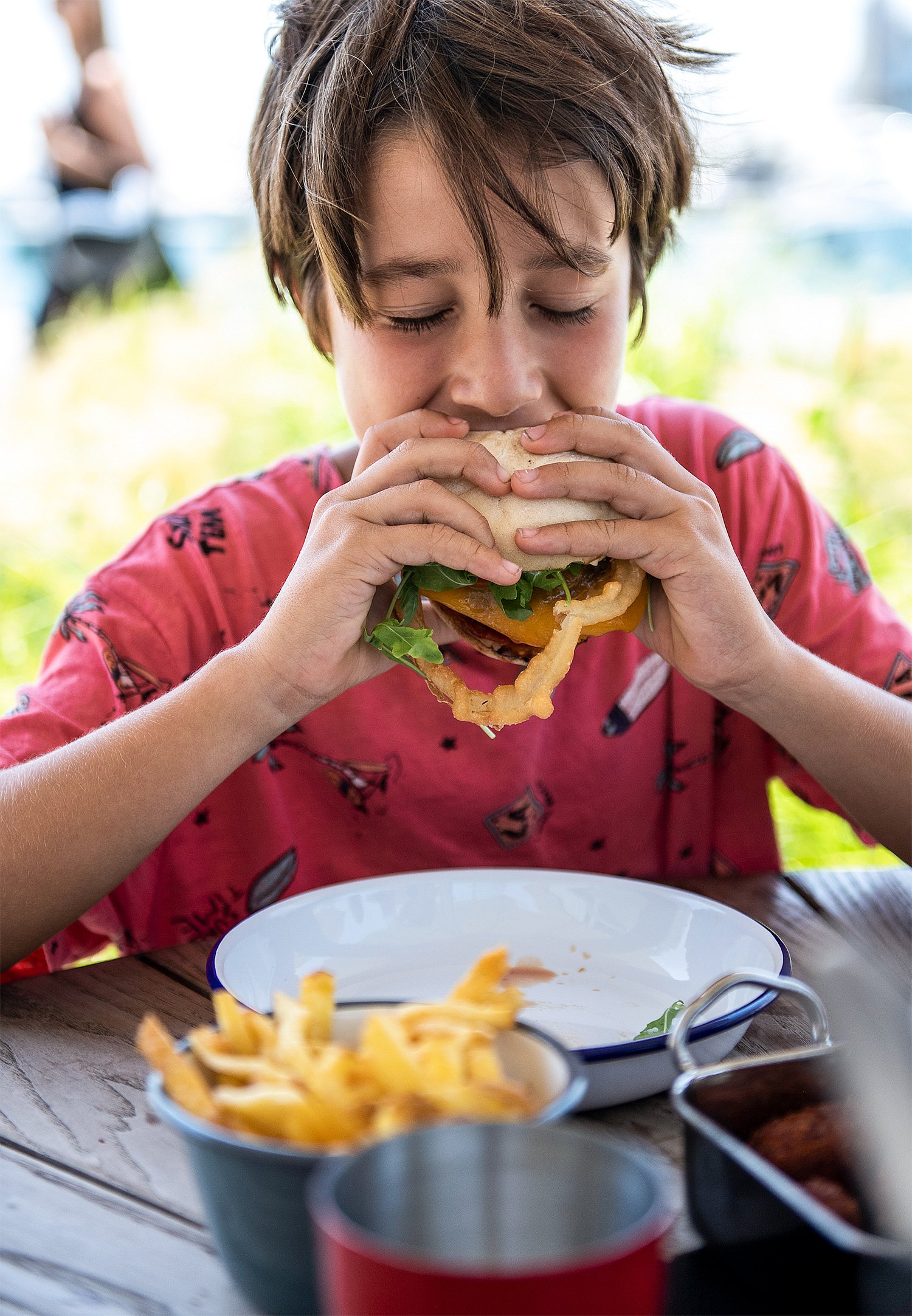 "Boy in red shirt enjoying his hamburger on his comfortable Pantagruel bench."