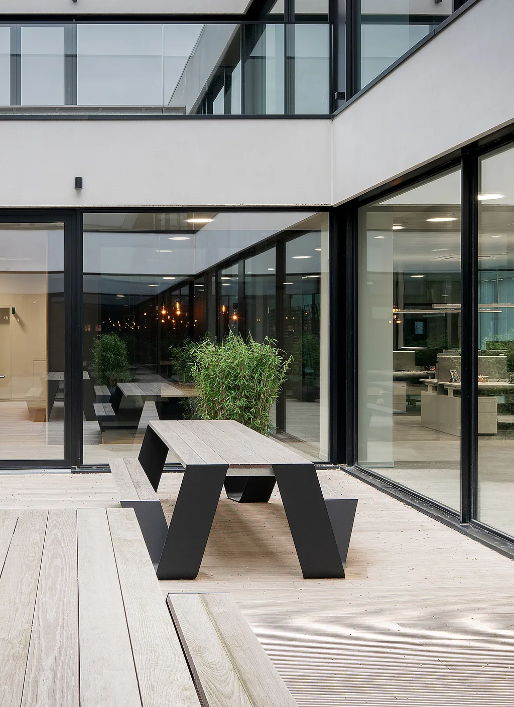 Modern kantoorinterieur met grote ramen van vloer tot plafond en een open patio met houten Hopper picknicktafels waar medewerkers buiten in het gebouw kunnen werken.