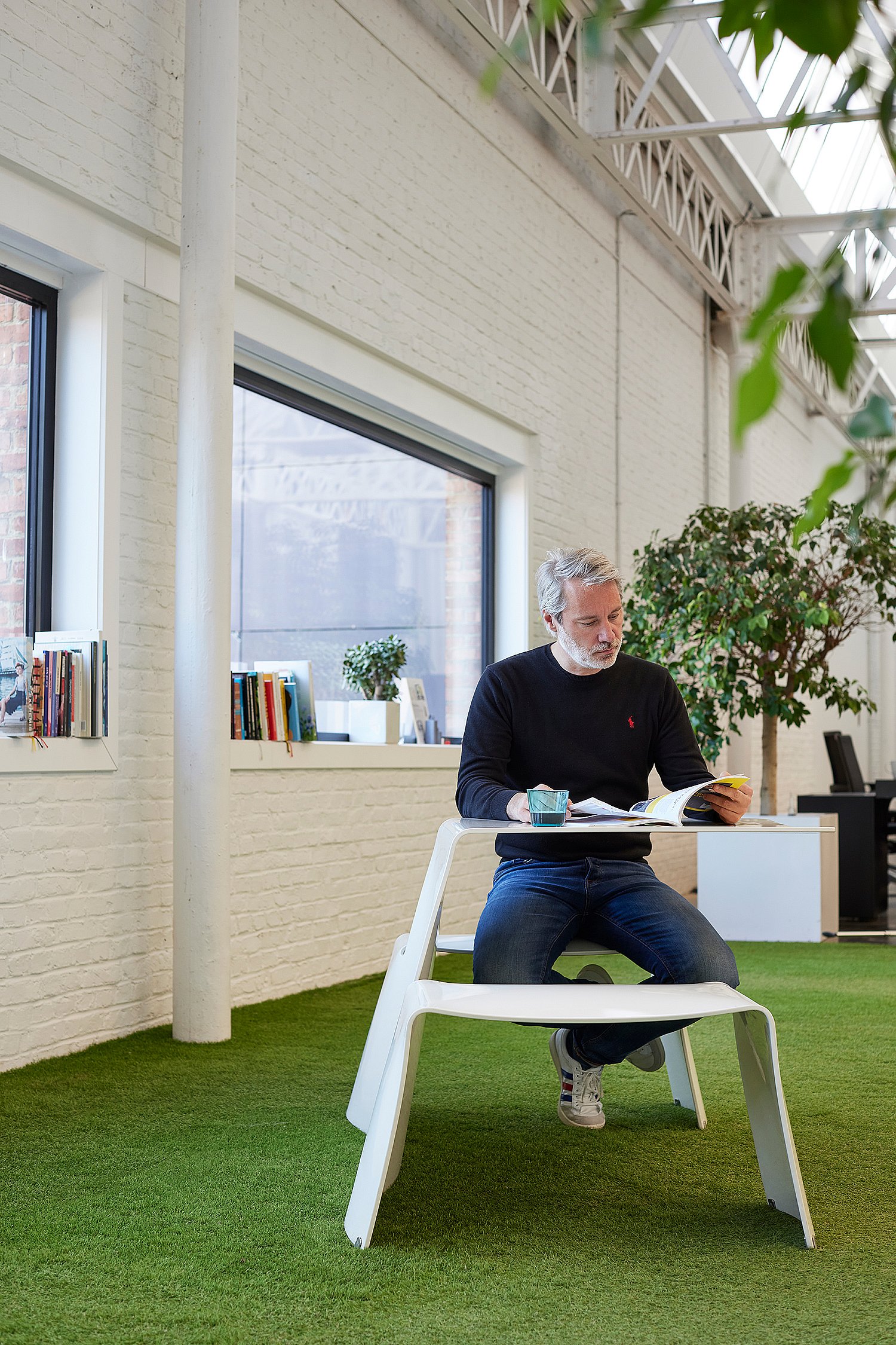 “Mann liest an einem weißen Picnik-Tisch auf einem Stück Innengras im hellen Industriebüro.”