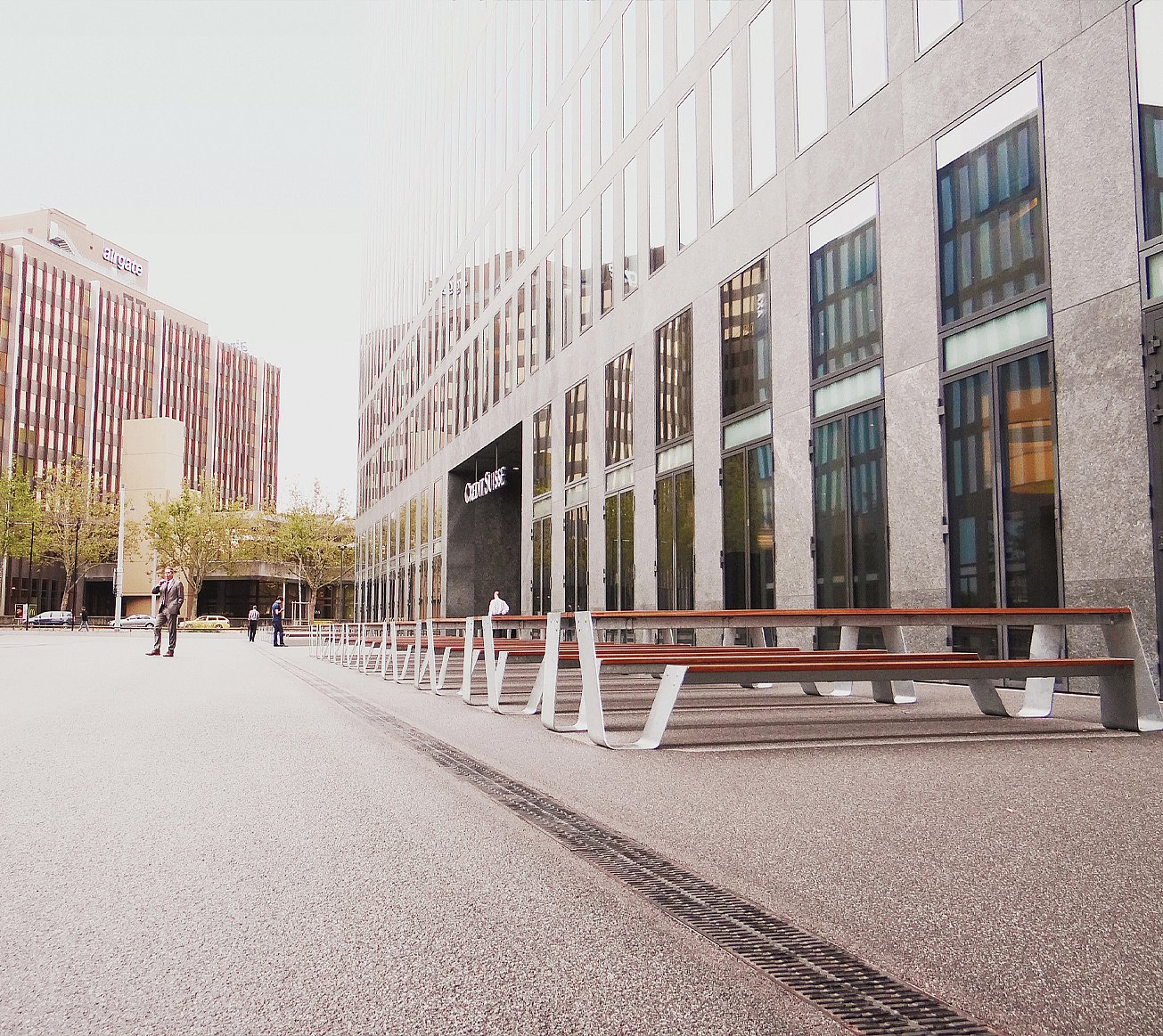 “Long row of white Hopper picnic tables lined up in an urban plaza beside the Credit Suisse tower in Zürich, with the glass-and-steel high-rise rising in the background.”
