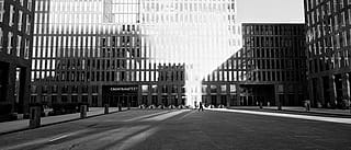 « Plan extérieur large de l’esplanade de la tour du Credit Suisse, où une ligne répétée de tables Hopper structure l’espace public entre des bâtiments contemporains. »