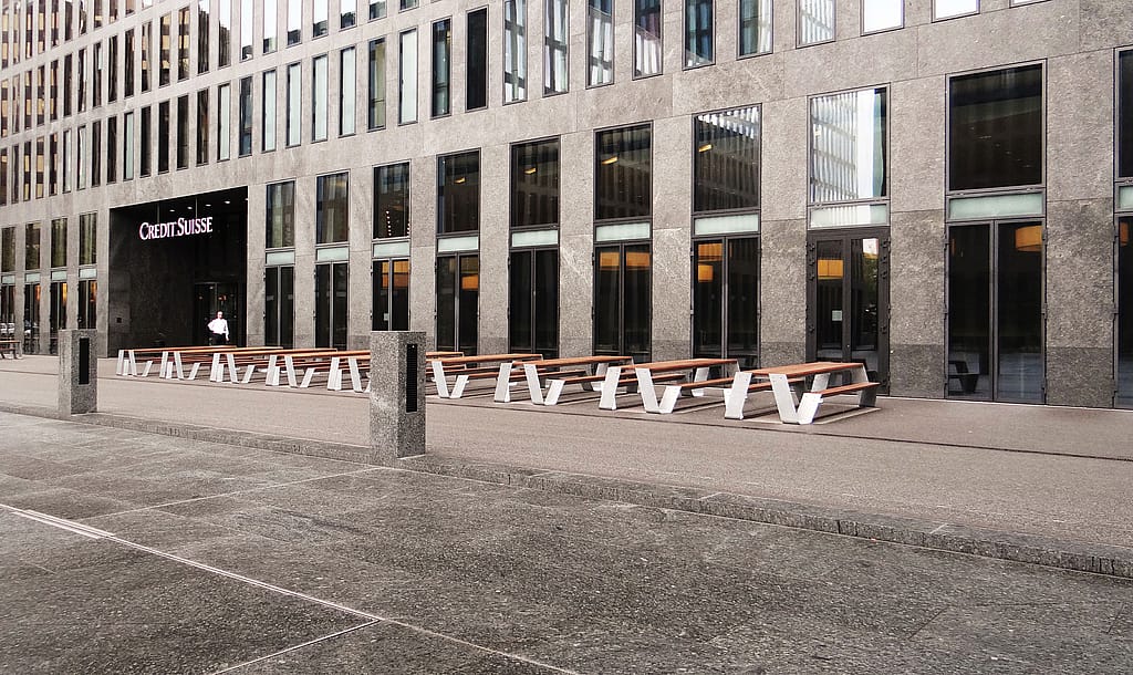 « Place publique avec plusieurs tables de pique-nique Hopper blanches disposées en ligne droite, créant des sièges généreux devant les tours de bureaux modernes. »