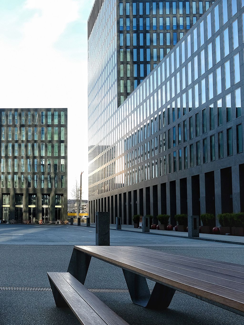« Immeuble de bureaux moderne avec façade en verre réfléchissant dominant la zone de sièges extérieure dans le quartier d’Oerlikon à Zurich. »
