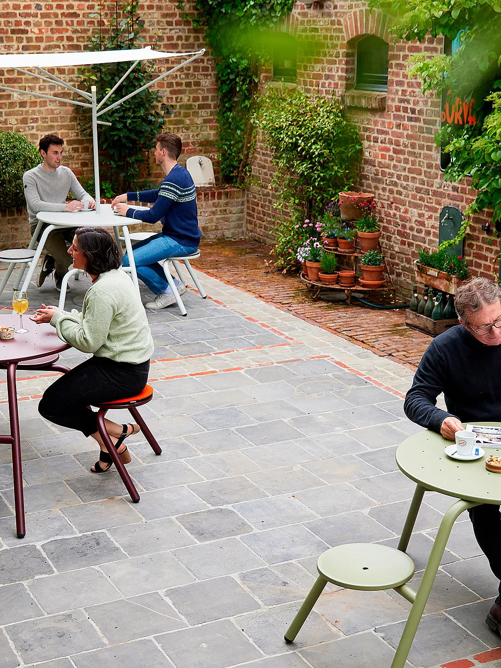 Eklektische Terrasse des Restaurants De Barbier in Dranouter, wo moderne Gartenmöbel einen Kontrast zum rustikalen Charakter des alten Backsteingebäudes bilden.