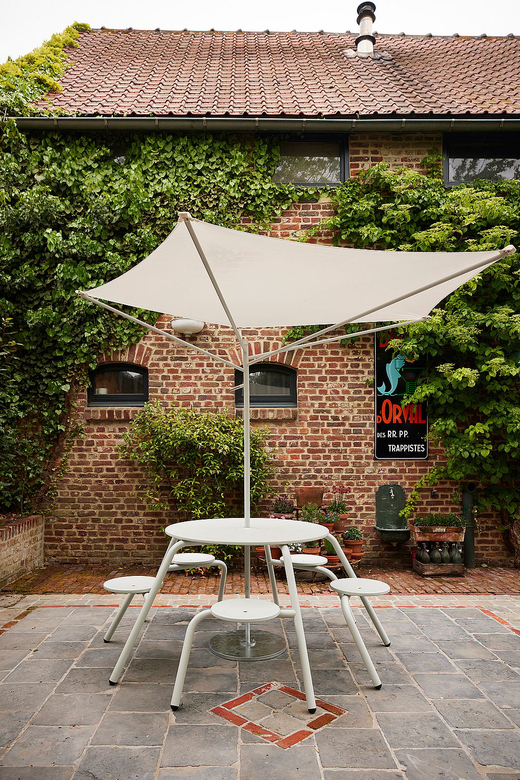 “High tiki tables with matching bar stools on a terrace next to a traditional brick facade, creating an informal space for drinks and conversations. ”