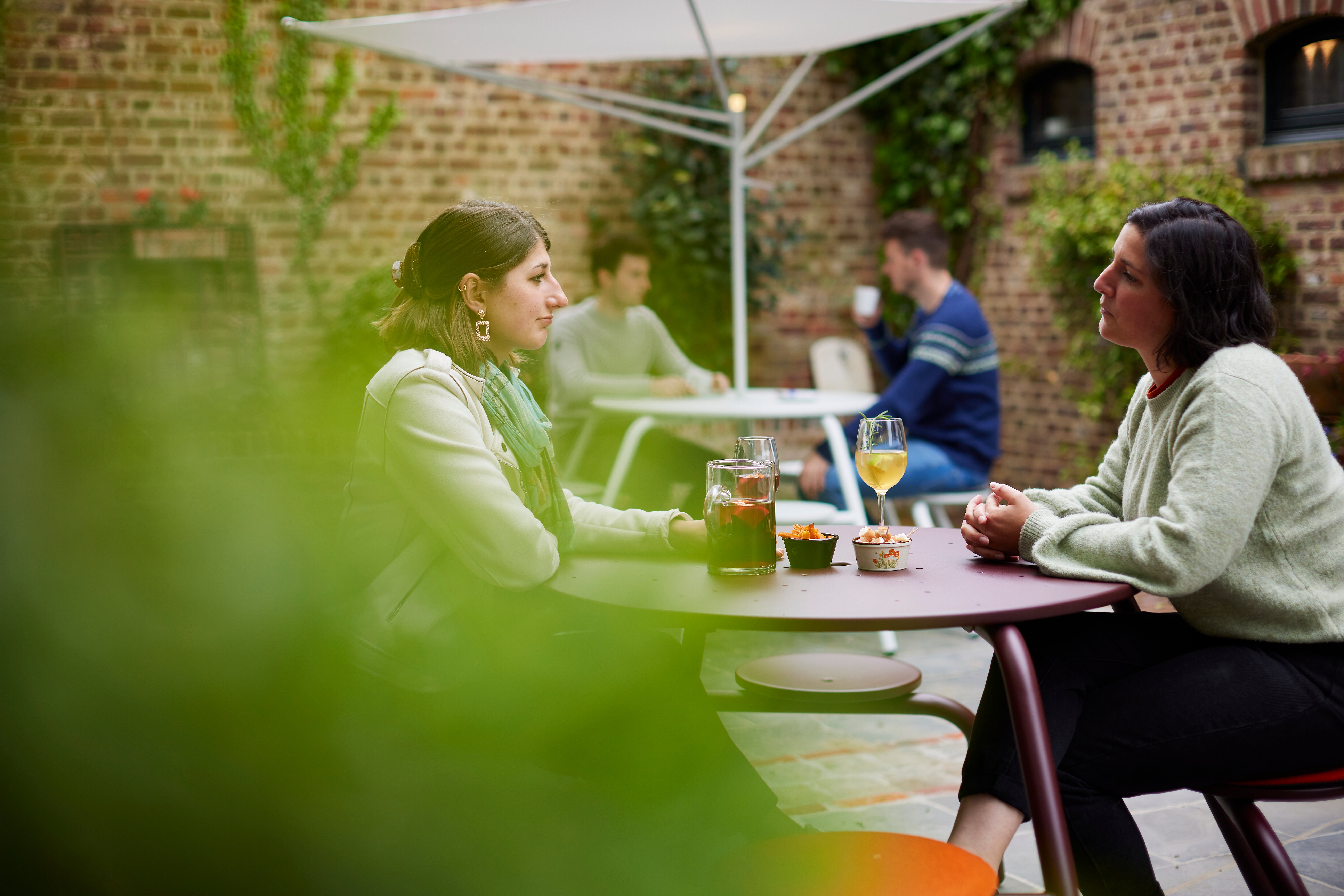 “Guests tell stories about virus tables in a hidden courtyard shaded by an acacia roof. ”