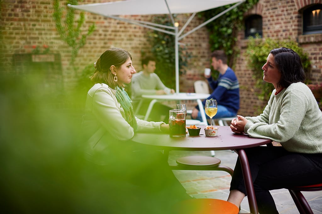 “Guests tell stories about virus tables in a hidden courtyard shaded by an acacia roof. ”