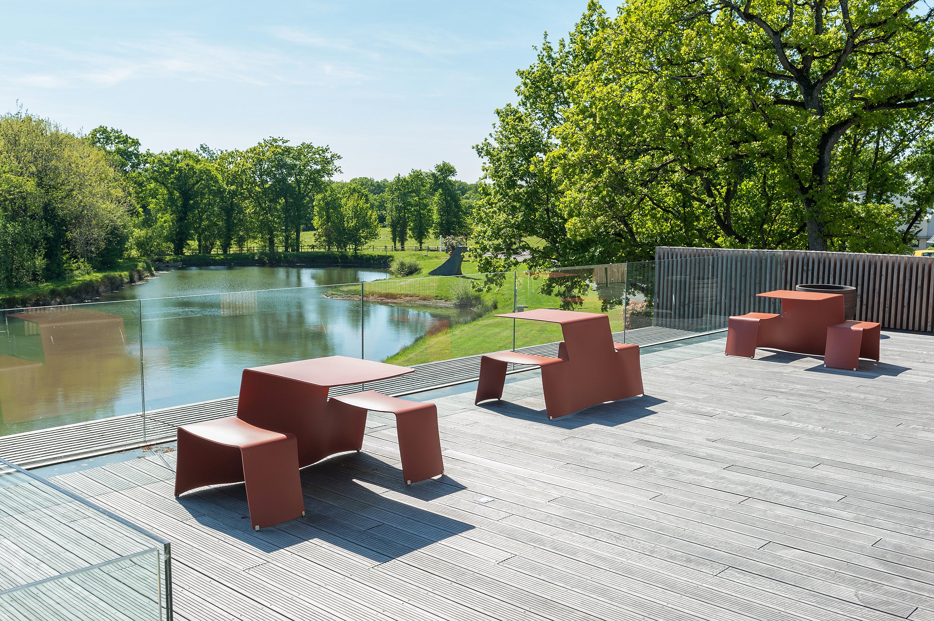Terracotta Picnik tafels en banken op een houten dakterras met uitzicht op een rivier en bomen.