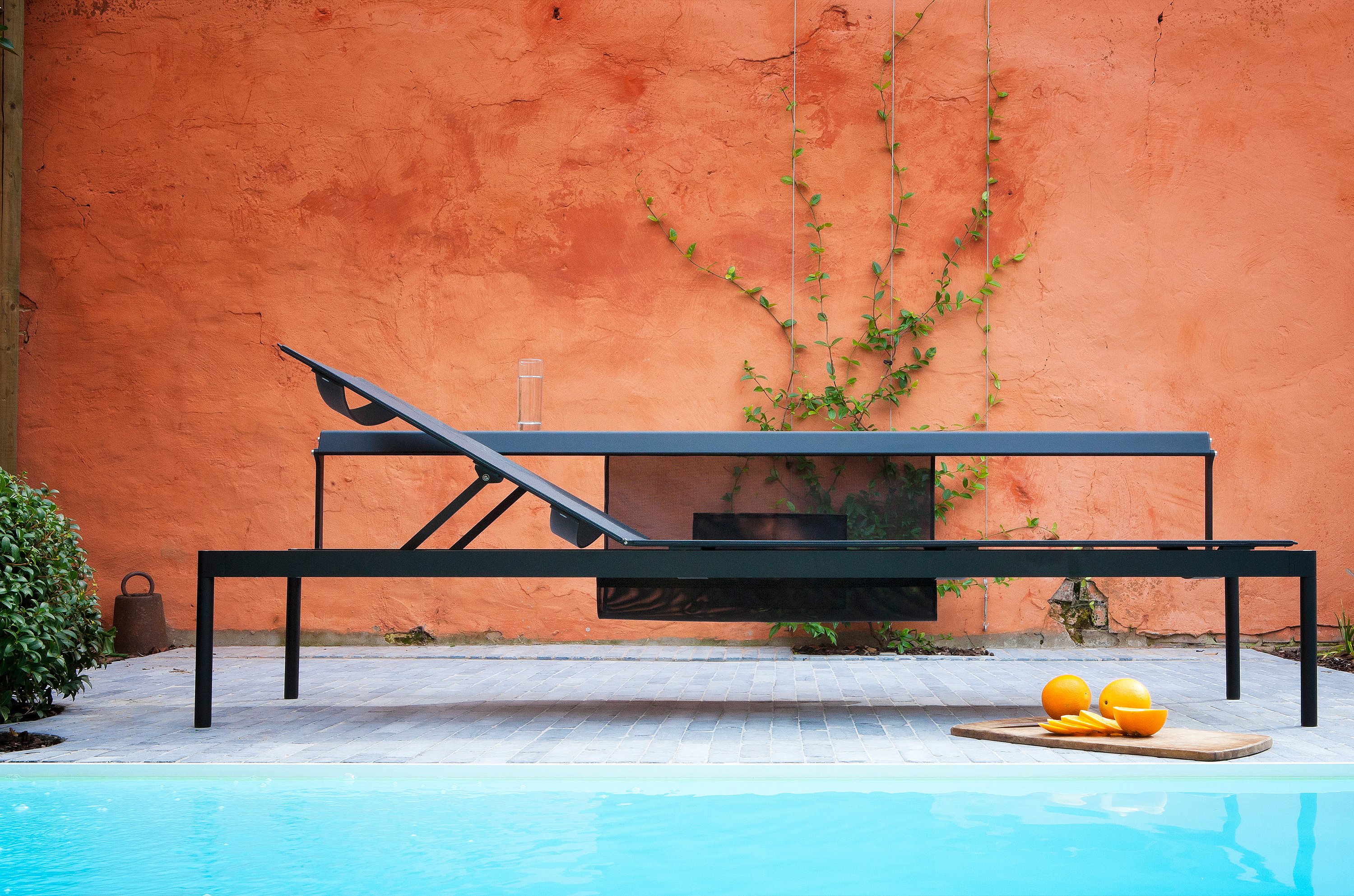   Seitenansicht einer schwarzen Sol&Luna-Liege, die zu einem Tagesbett umfunktioniert wurde. Die verstellbare Rückenlehne ist hochgeklappt, im Vordergrund ist ein Swimmingpool zu sehen.