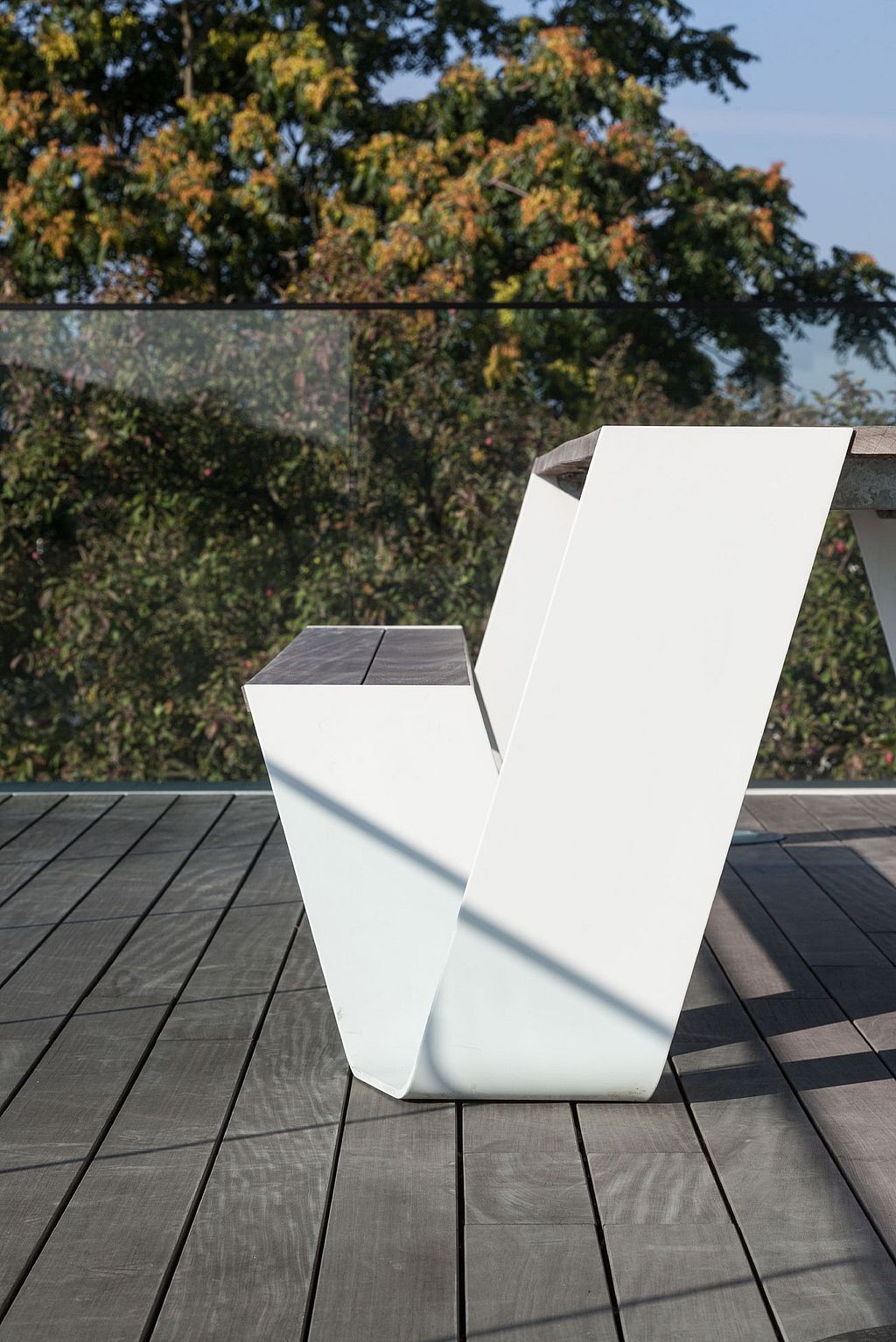 Side profile of a white Hopper picnic table with wooden seat and tabletop on a balcony terrace, with trees visible beyond the glass balustrade.