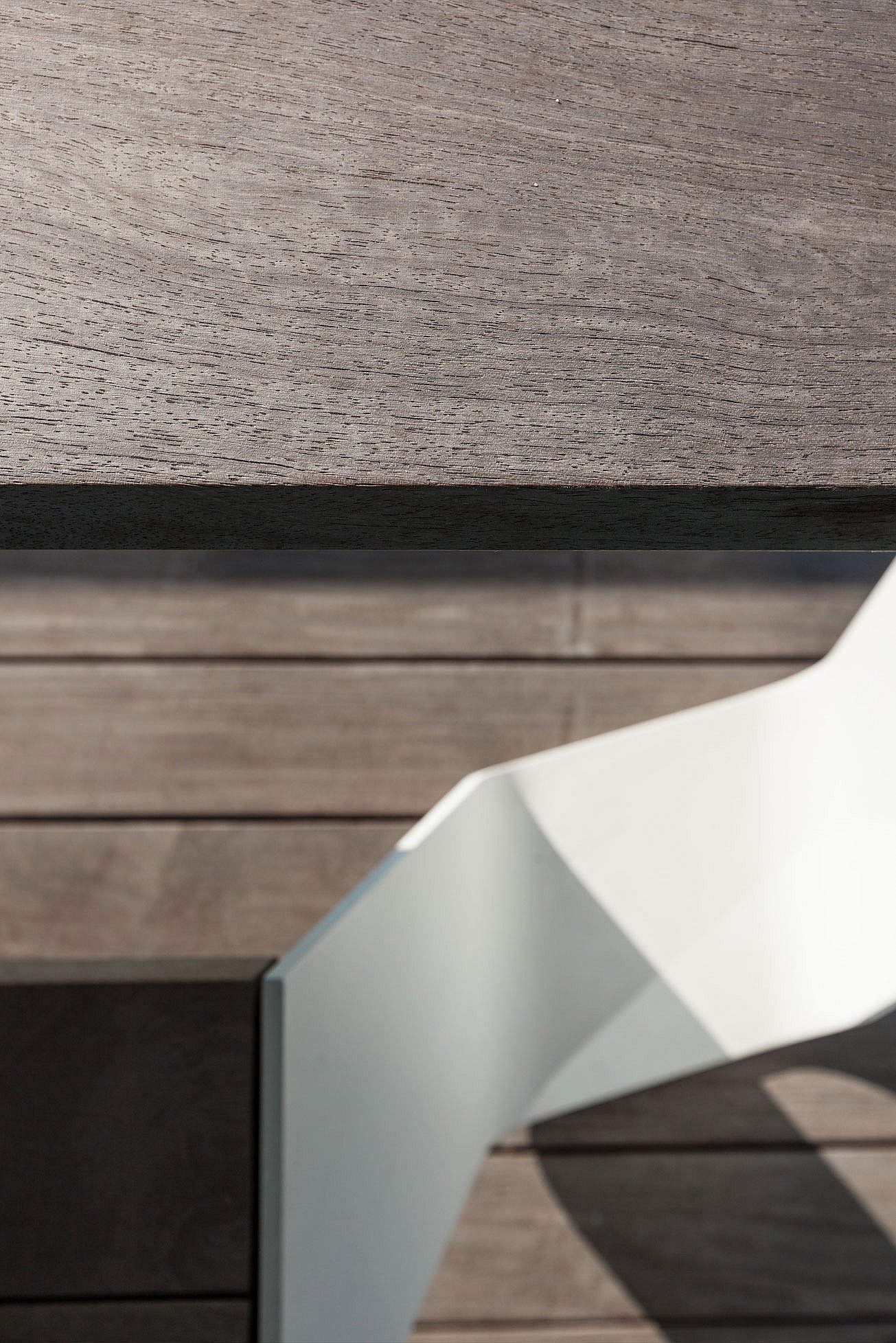 Gros plan d’une table Hopper montrant le bord de dessus de table en bois foncé et le pied en aluminium blanc plié contre le revêtement en bois assorti.