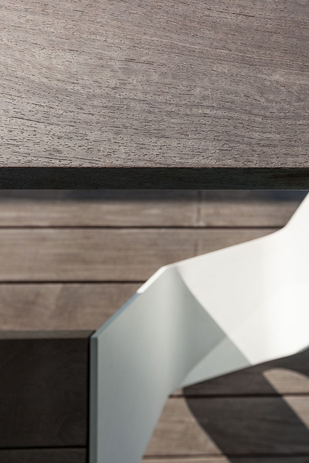 Gros plan d’une table Hopper montrant le bord de dessus de table en bois foncé et le pied en aluminium blanc plié contre le revêtement en bois assorti.