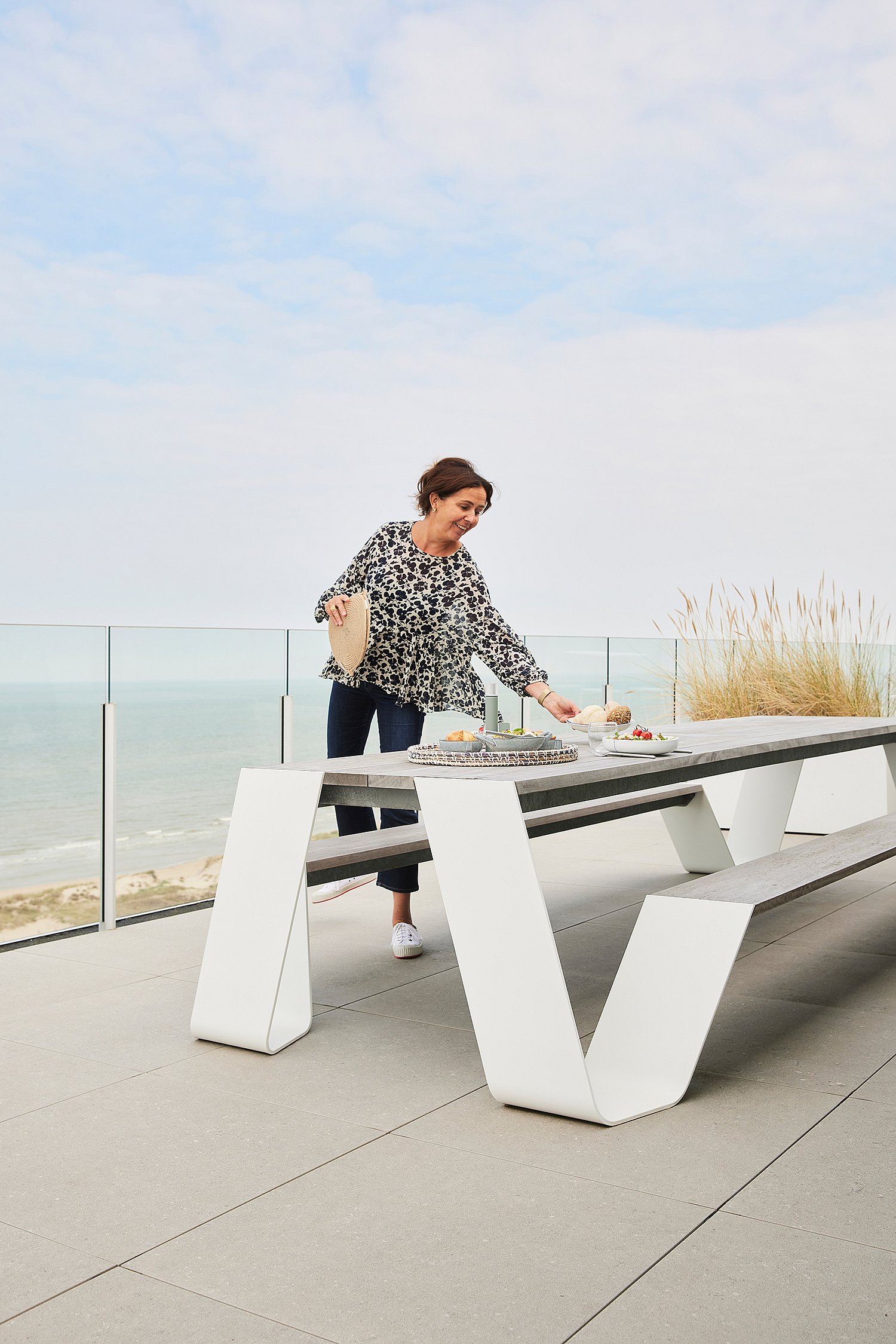 Vrouw met een lunchtafel aan zee op een witte hoptafel op een ruim terras met uitzicht op het strand en de zee.