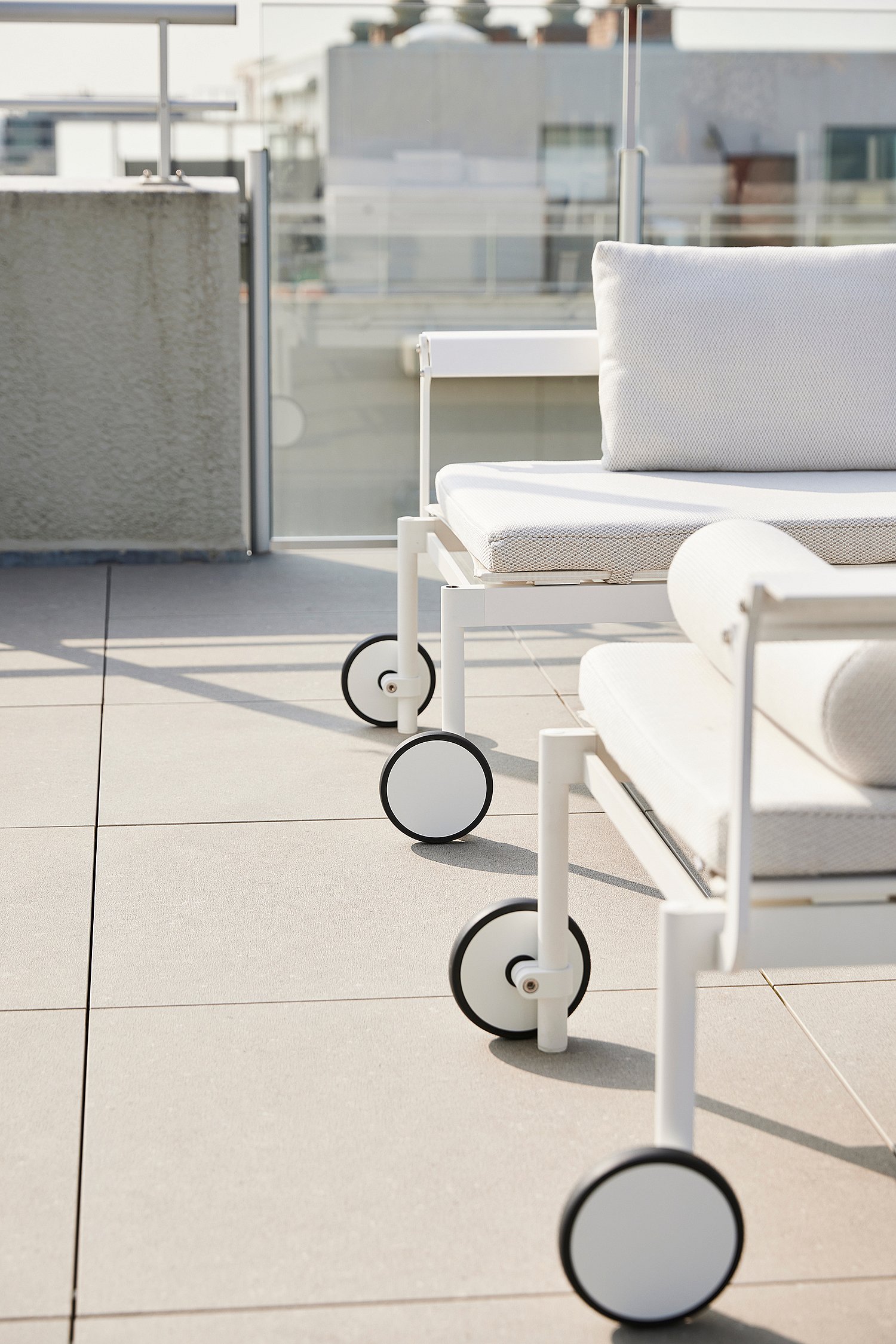 Close-up van de ronde wielen en het witte frame van Sol + Luna ligstoelen op een zonovergoten dakterras.