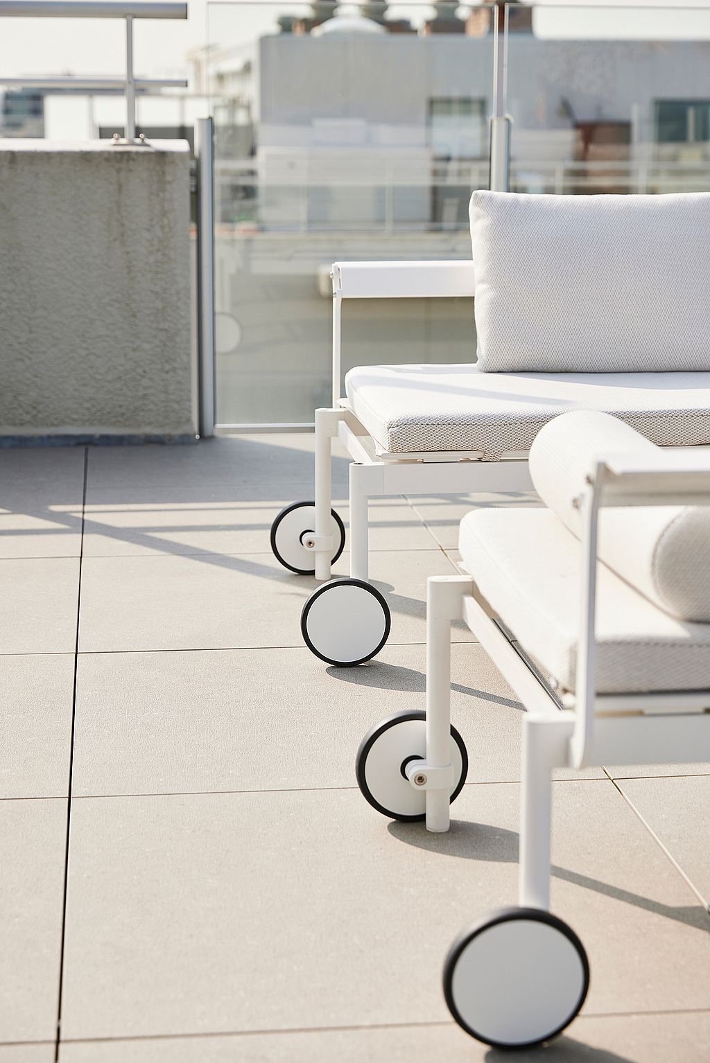 Close-up van de ronde wielen en het witte frame van Sol + Luna ligstoelen op een zonovergoten dakterras.