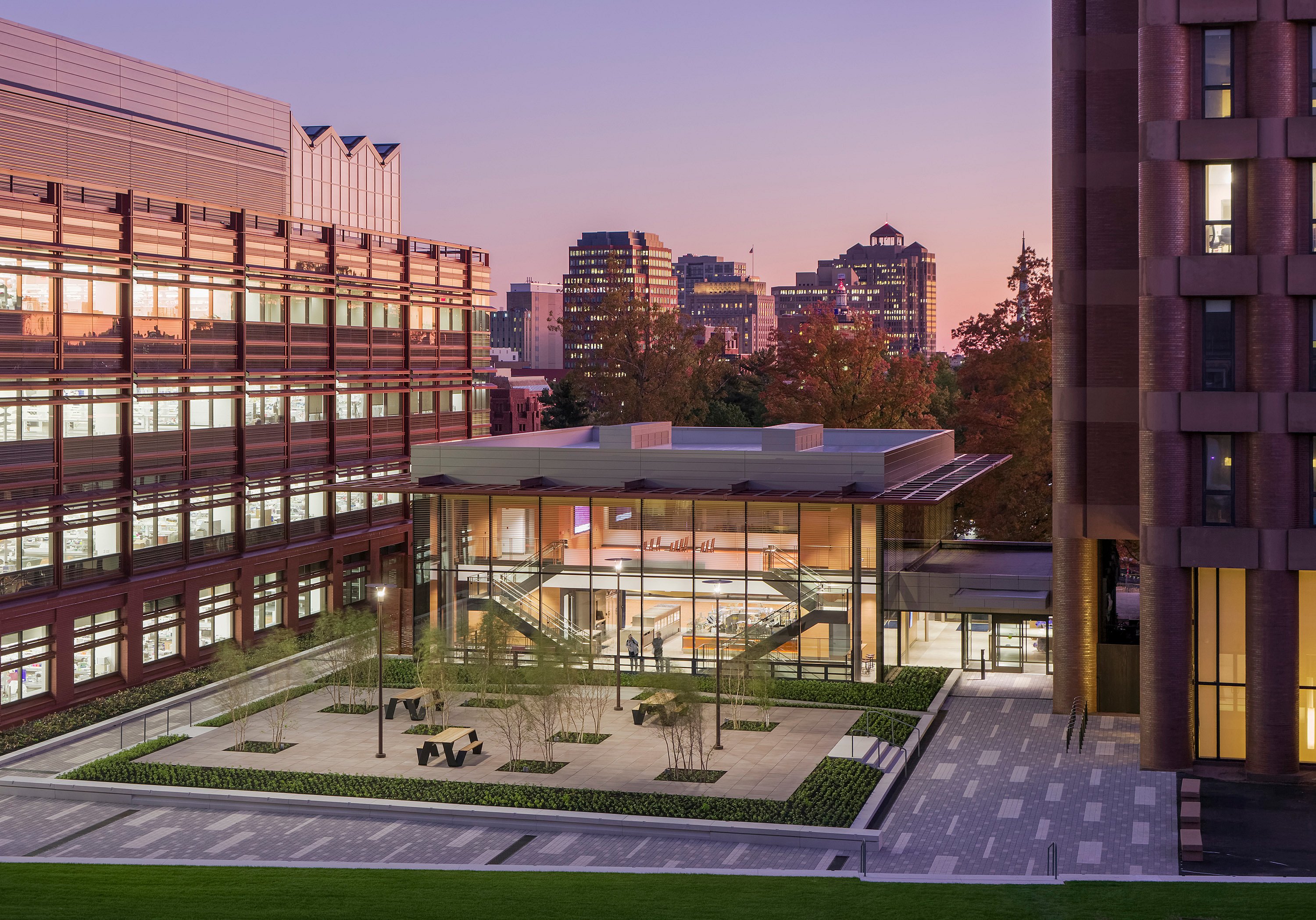   Tagesaufnahme des Vorplatzes des Yale Science Building aus erhöhter Perspektive. Zu sehen sind der gläserne Pavillon, der bepflanzte Innenhof und die schwarzen Hopper-Picknicktische, eingebettet zwischen den umliegenden Universitätsgebäuden und herbstlich gefärbten Bäumen.