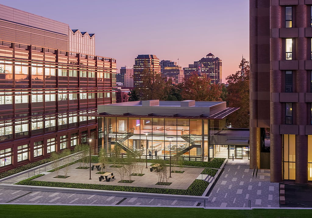 Tagesaufnahme des Vorplatzes des Yale Science Building aus erhöhter Perspektive. Zu sehen sind der gläserne Pavillon, der bepflanzte Innenhof und die schwarzen Hopper-Picknicktische, eingebettet zwischen den umliegenden Universitätsgebäuden und herbstlich gefärbten Bäumen.