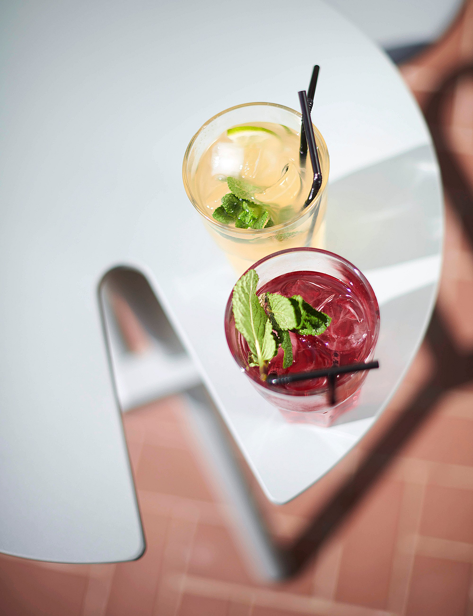 Top-down detail of two refreshing drinks on the rounded pale blue Bistroo table, framed by the integrated seats and brick paving below.
