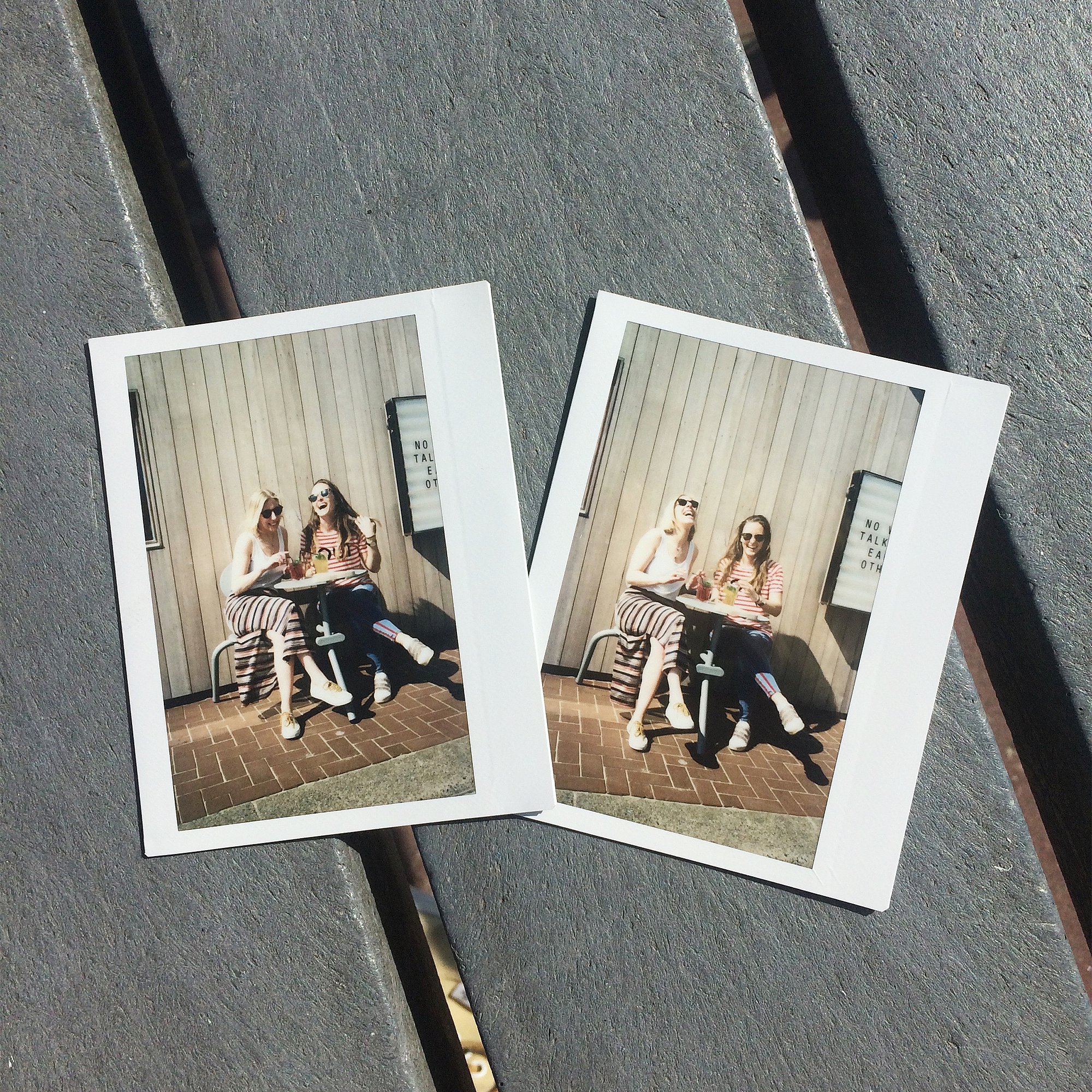 Two instant photos lying on a slatted tabletop, each showing two women sitting together at the Bistroo set outside the restaurant.