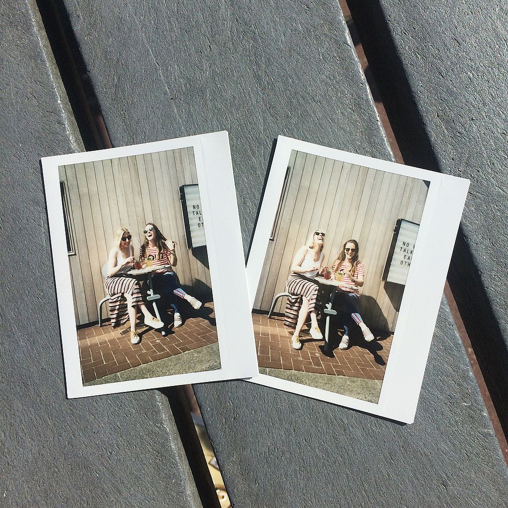 Two instant photos lying on a slatted tabletop, each showing two women sitting together at the Bistroo set outside the restaurant.