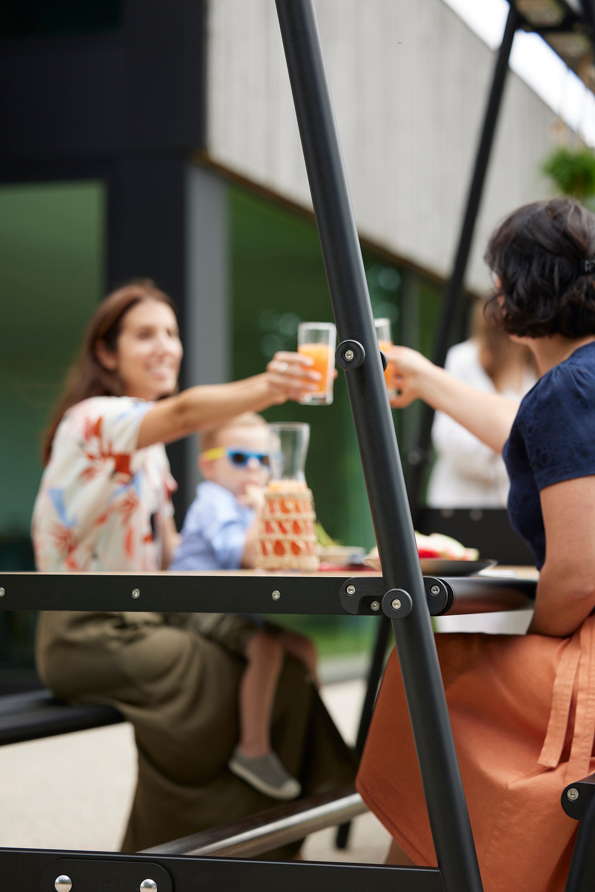   Trois adultes et un enfant trinquent autour de la table AMAi, où sont disposés une carafe et des amuse-gueules d'été.