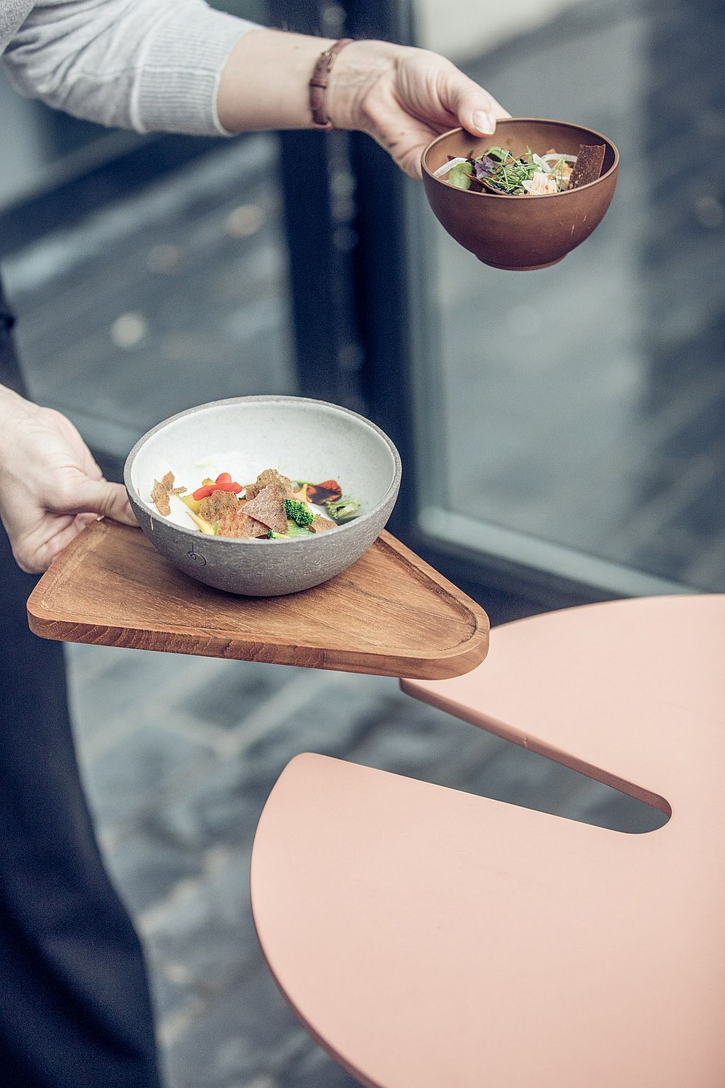 Close-up van een server met twee kommen terwijl een driehoekige houten lade wordt gebruikt om de kloof tussen de zij-aan-zij Bistroo-stoelen te overbruggen.