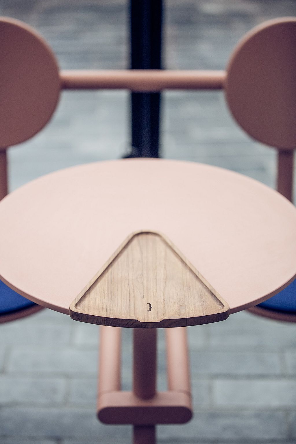 Close-up van het ronde roze Bistroo tafelblad met een driehoekige houten serveerschaal netjes in het midden uitgesneden tussen de twee stoelen.