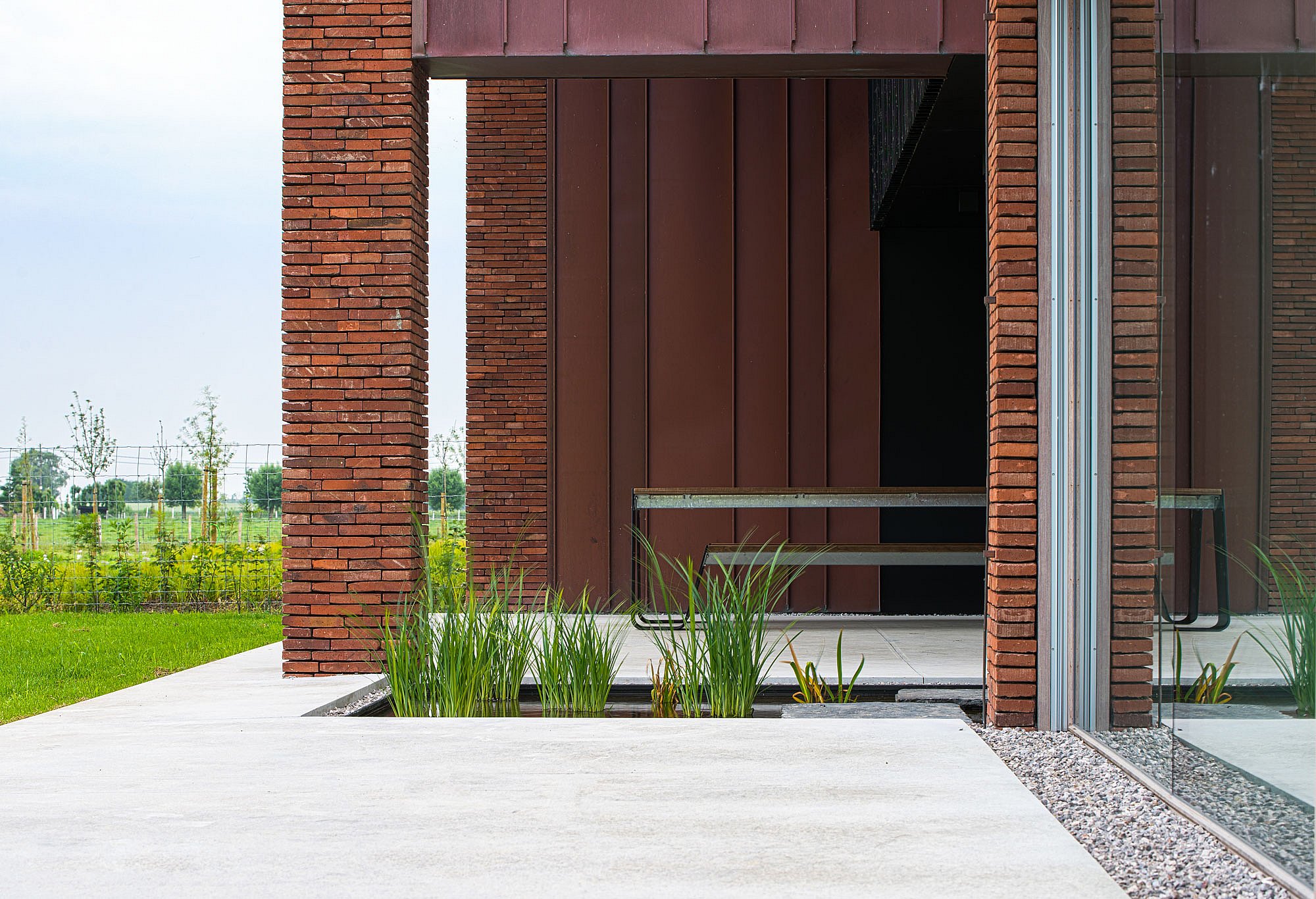Hopper picnic table beside a brick-and-copper façade, with ornamental grasses planted along the edge of the pale concrete terrace.”