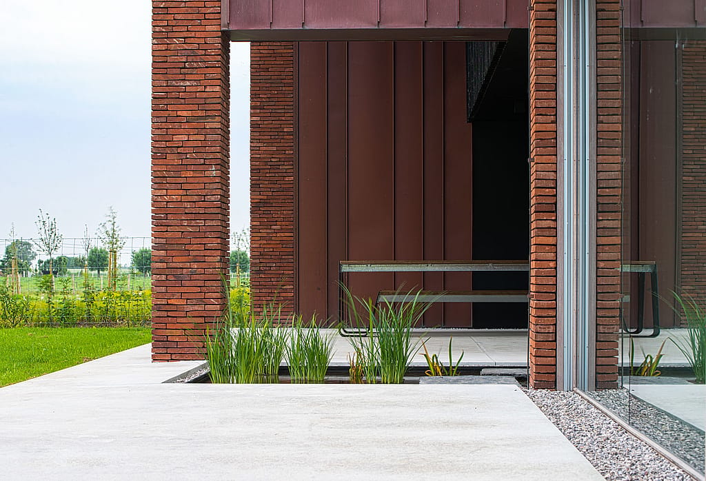 Hopper picnic table beside a brick-and-copper façade, with ornamental grasses planted along the edge of the pale concrete terrace.”
