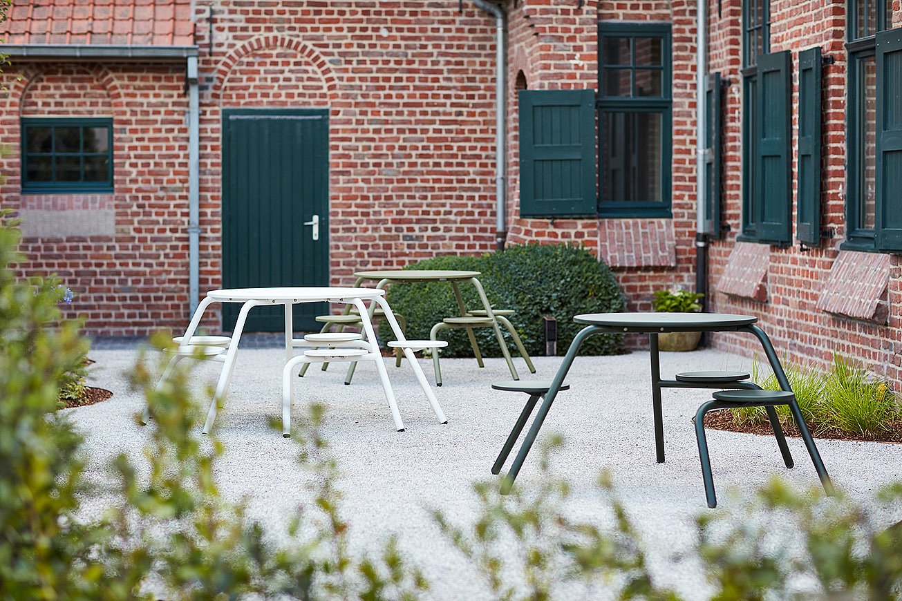 Playful outdoor setting with colorful Virus tables inviting children and adults to sit together in a cheerful holiday-house garden.