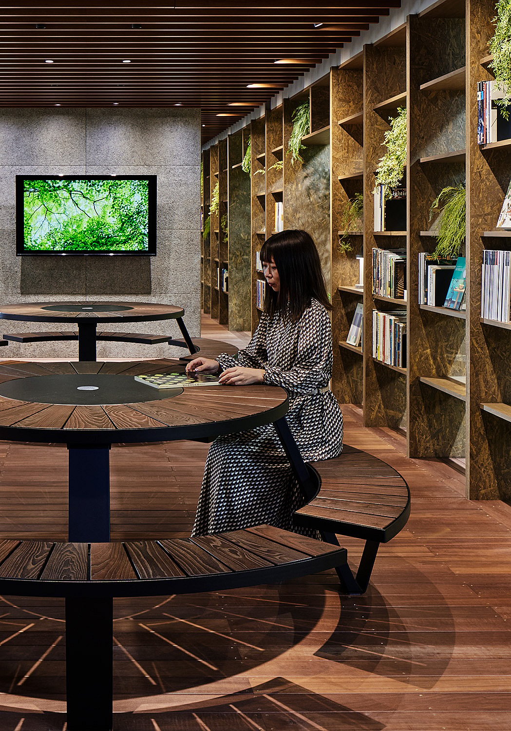 Salon de bureau biophilique à Tokyo avec une table de pique-nique ronde Pantagruel placée parmi une végétation abondante, des finitions en bois chaleureux et une architecture intérieure doucement éclairée.
