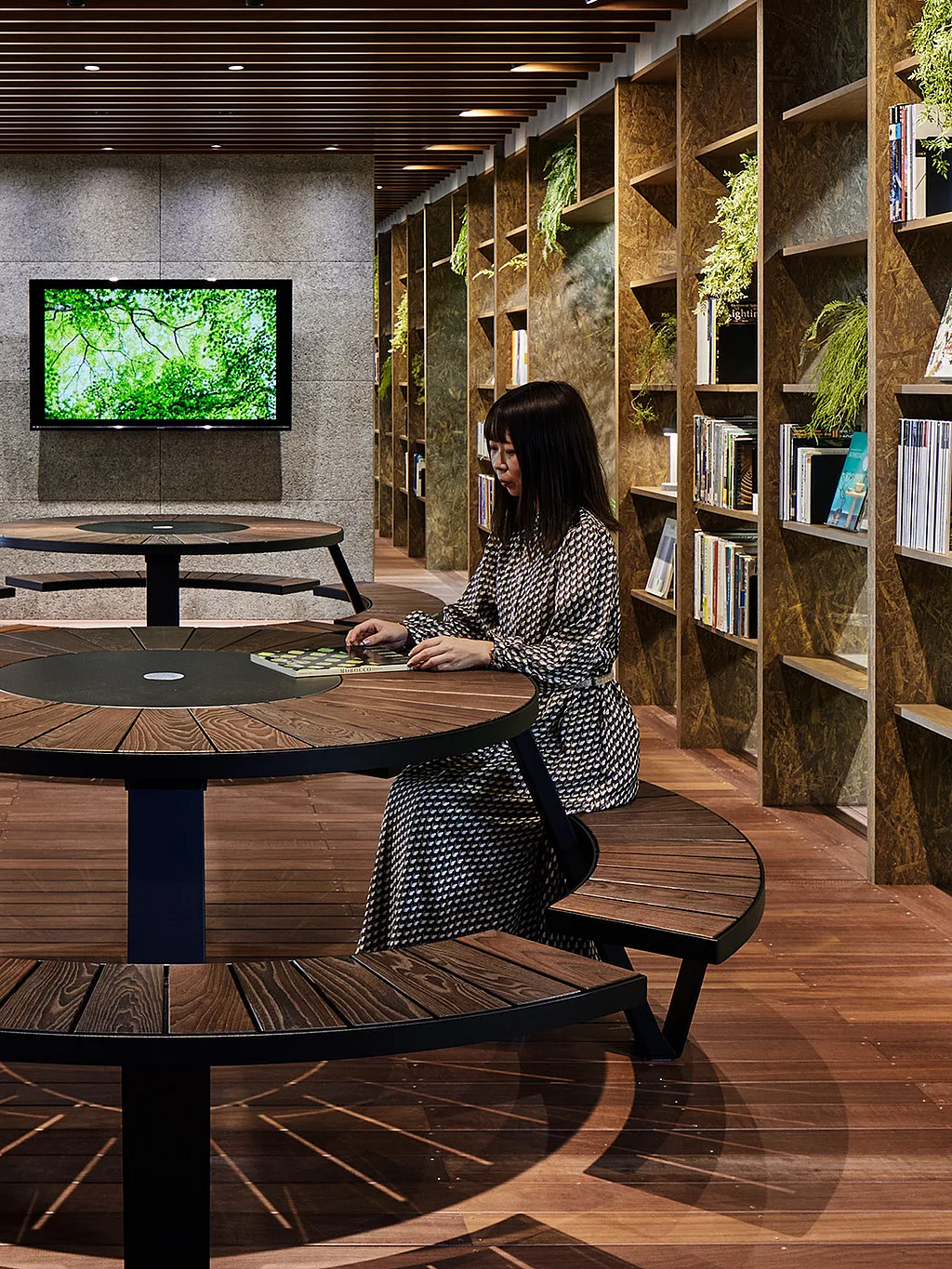 Biophilic office lounge in Tokyo with a round Pantagruel picnic table set among abundant greenery, warm wood finishes, and softly lit interior architecture.