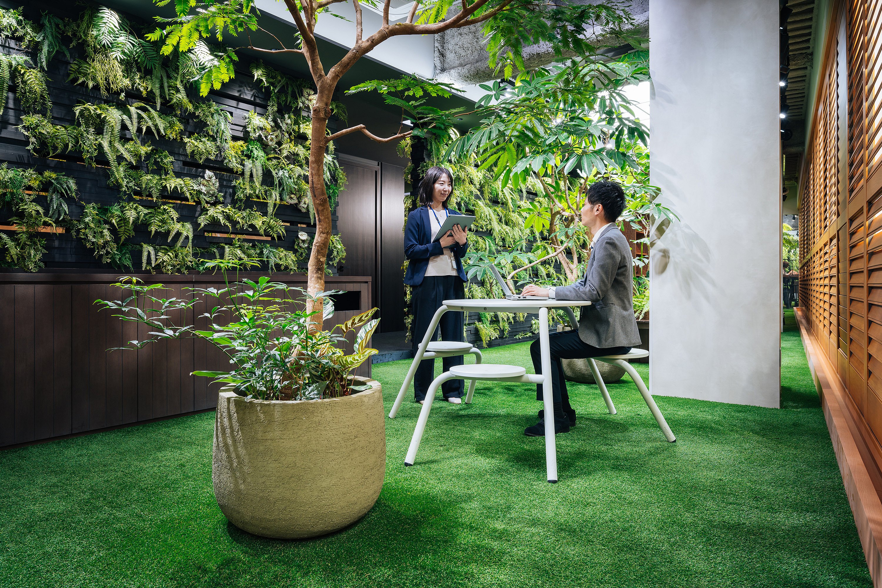 Ruhiger Büro-Retreat mit dichter Bepflanzung, natürlichen Texturen und einem runden Virentisch, der das Interieur eher wie einen Garten als wie einen Arbeitsplatz wirken lässt.