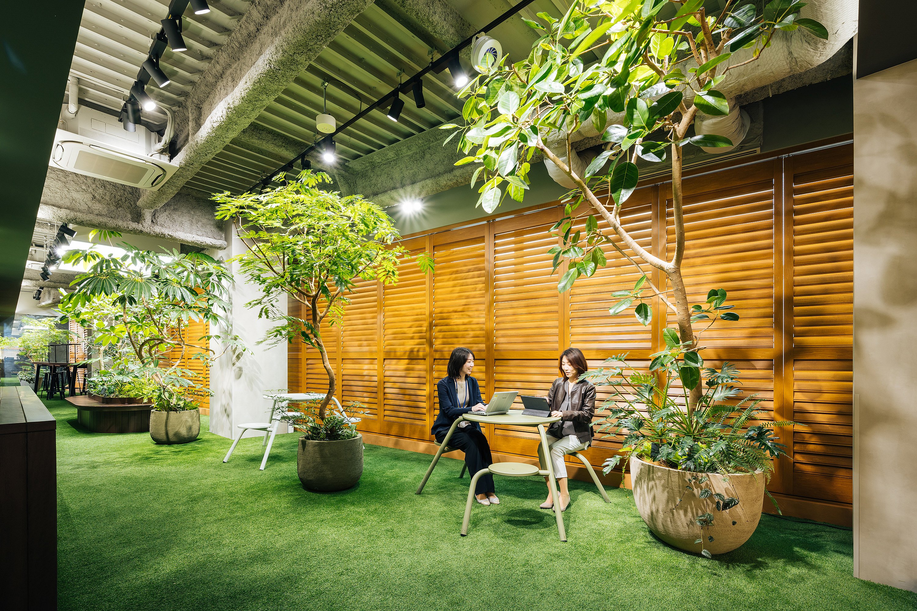 Ruhiger Büro-Retreat mit dichter Bepflanzung, natürlichen Texturen und einem runden Virentisch, der das Interieur eher wie einen Garten als wie einen Arbeitsplatz wirken lässt.