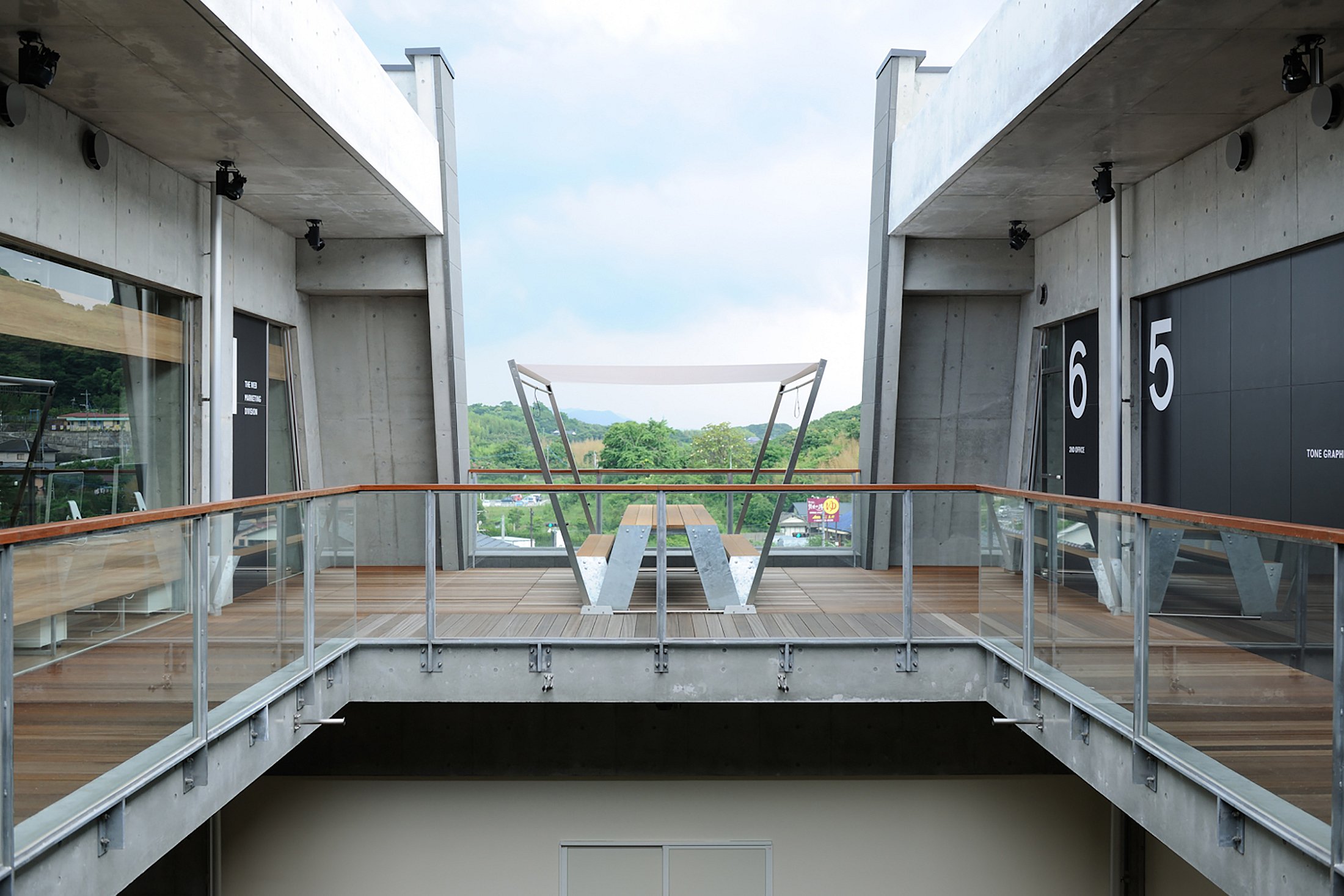 Atrium ouvert symétrique au troisième étage avec une table de pique-nique Hopper centrée entre deux ailes en béton, encadrée par des rampes en verre et une vue lointaine sur la ville.