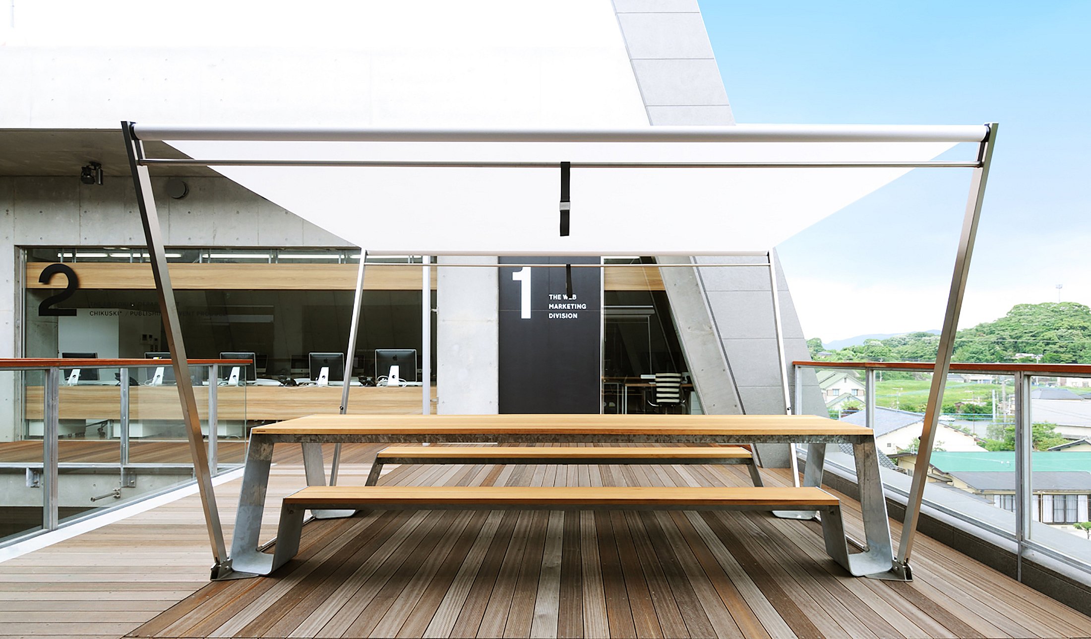 Table de pique-nique Hopper positionnée dans l’atrium aéré du niveau supérieur, offrant une vue dégagée sur la ville de Chikuho et un endroit lumineux et venteux pour s’asseoir.