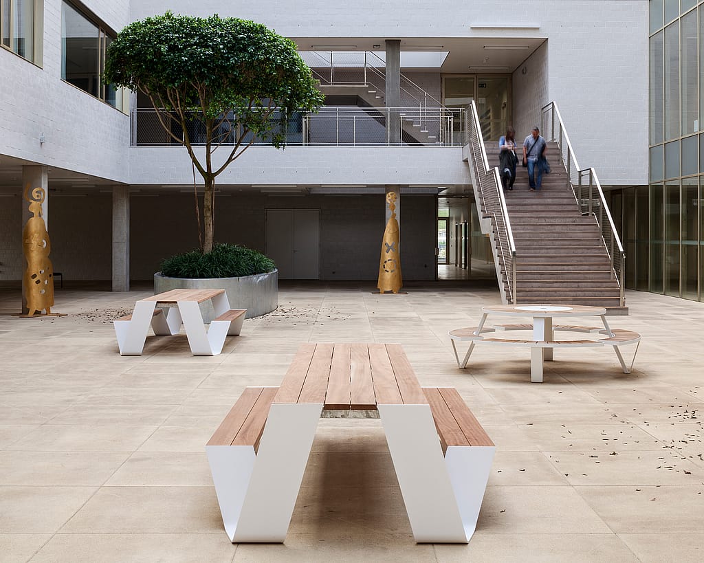 Ruhiger Indoor-Krankenhausgarten mit gemeinsamen Sitzgelegenheiten, Grün und Tageslicht, der Pflegearchitektur mit einem heimeligen Ort zum Innehalten und Verbinden kombiniert.