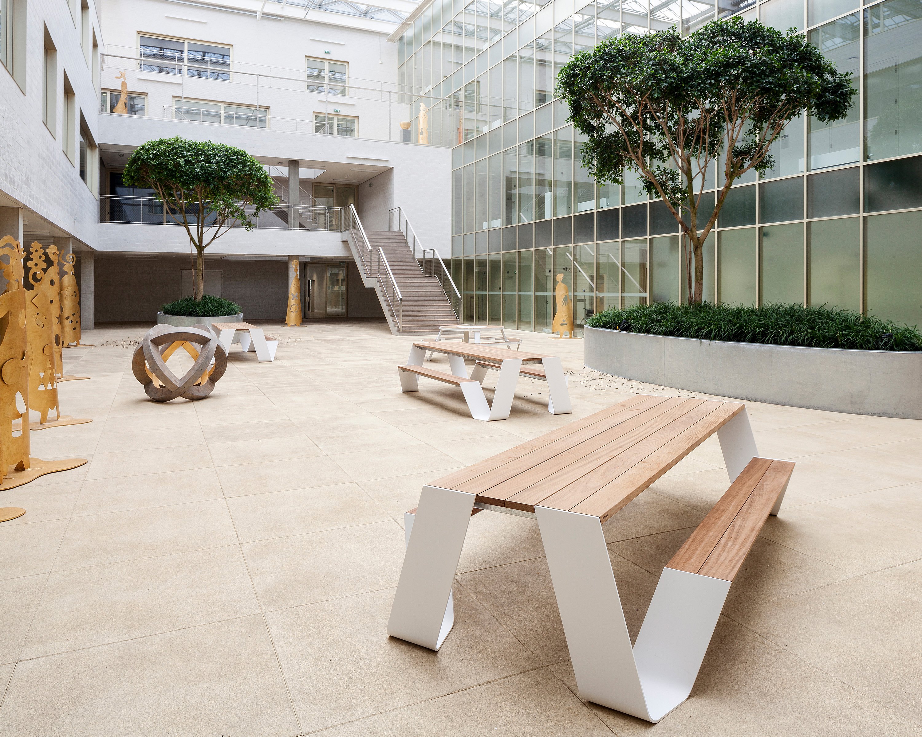 Extremis-Möbel in einem Wintergarten eines Krankenhauses, wo natürliches Licht und Bepflanzung dazu beitragen, einen ruhigen Gemeinschaftsbereich zu schaffen, der Ruhe und Erholung unterstützt.