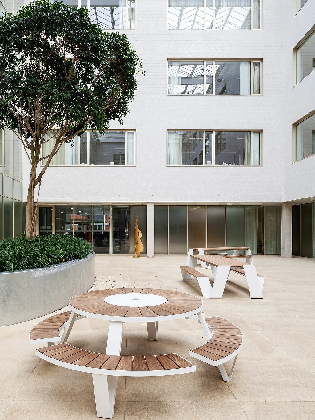 Bright hospital winter garden with Extremis outdoor-style furniture arranged among indoor planting, creating a calm shared space for patients, visitors, and caregivers.
