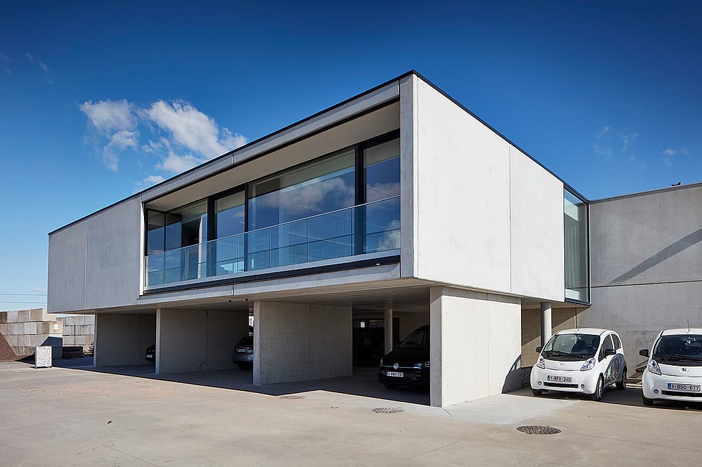 Ultramodernes Bürogebäude aus Beton mit großen Glasfenstern, einer vertieften Carport-Ebene und einem klaren blauen Himmel über dem Gravelart-Hauptquartier.