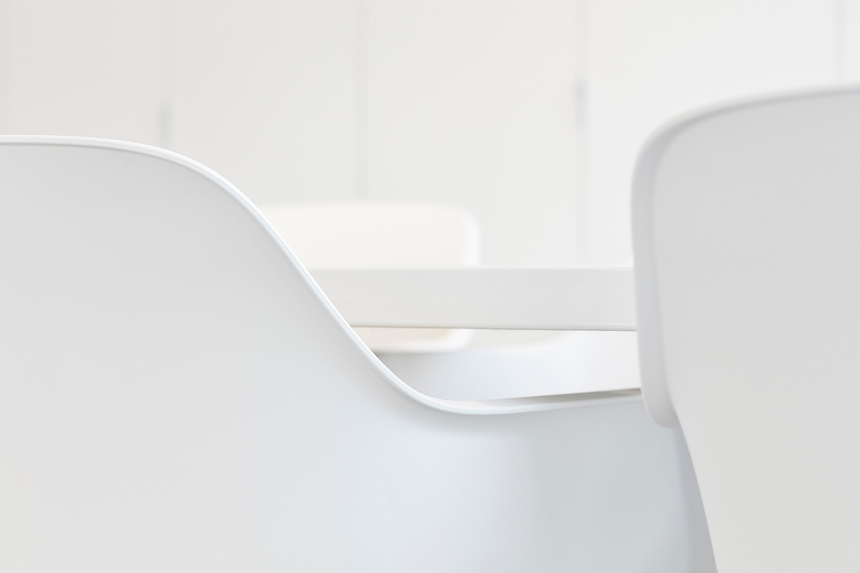 Minimale Nahaufnahme weißer Kapitänsstühle um einen weißen Tisch, wobei die glatten, geschwungenen Linien der Sitzgelegenheiten hervorgehoben werden.